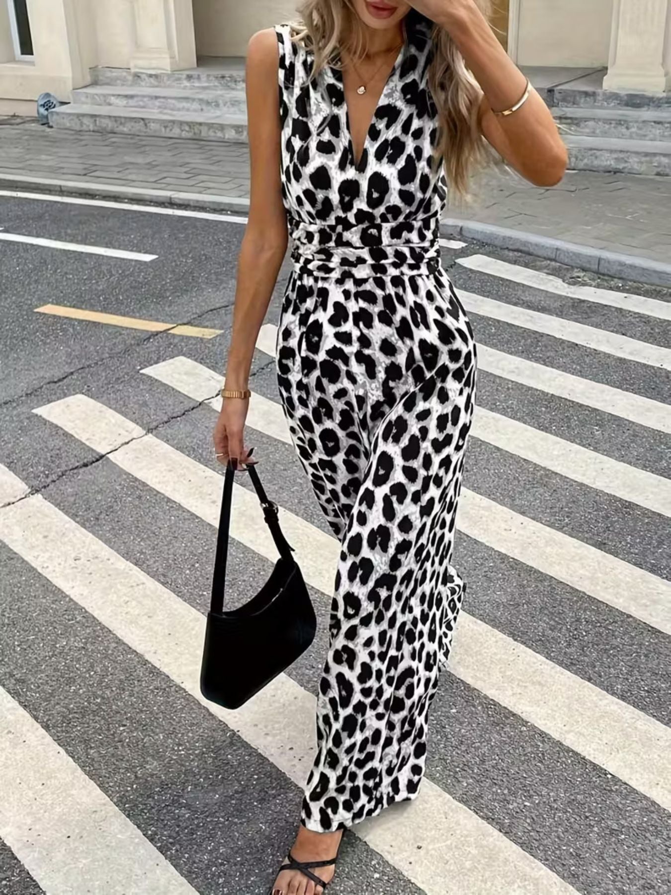 Woman wearing sleeveless leopard print jumpsuit, holding black handbag, crossing street