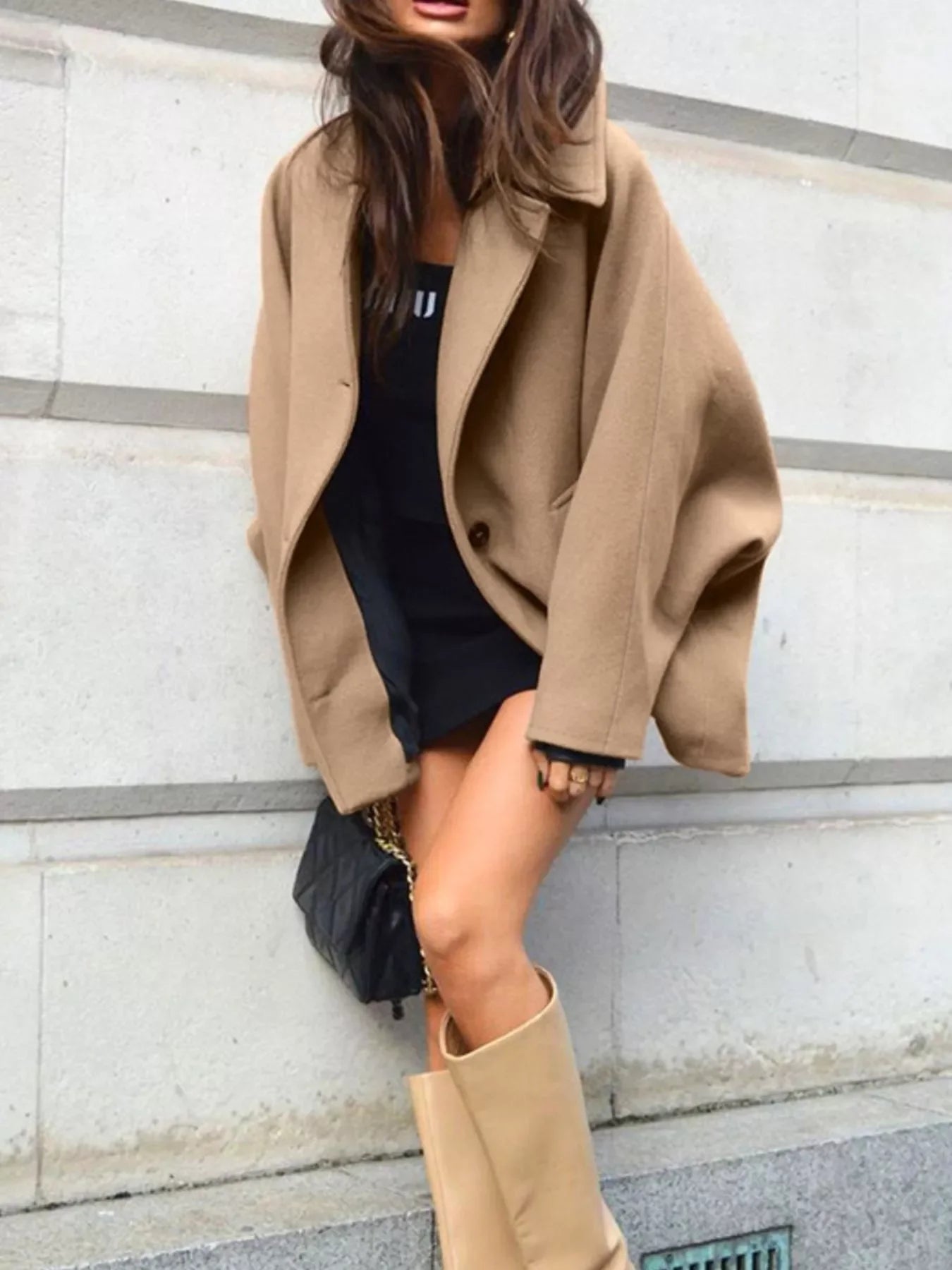 Woman wearing an oversized tan wool coat over a black mini dress and tan boots