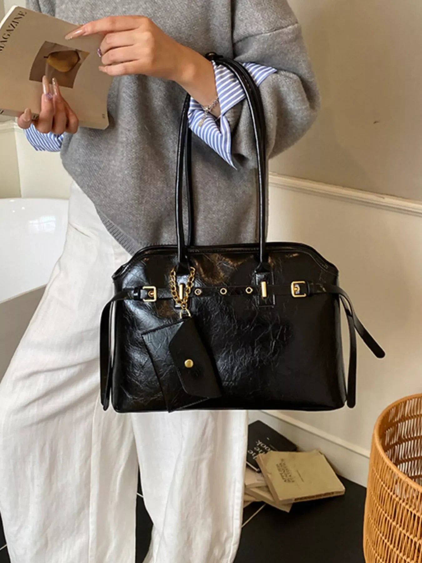 Woman holding black leather handbag with gold buckle details and attached pouch indoors