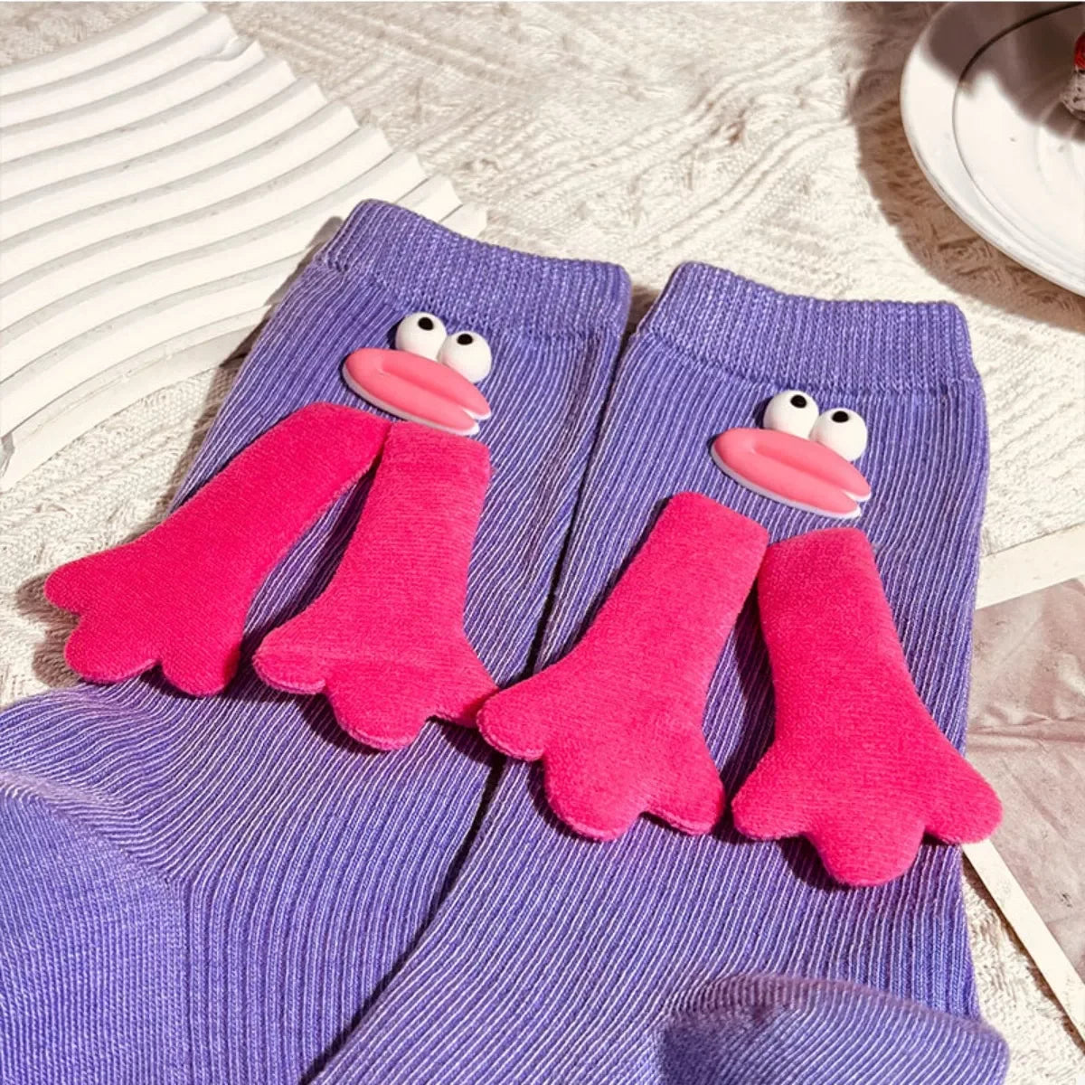 Purple ribbed socks with pink cartoon duck beak and feet decorations on a textured white surface