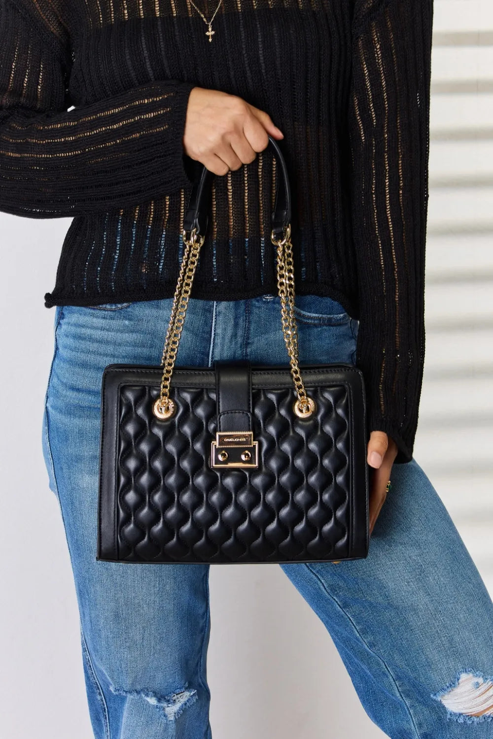 Woman holding black quilted handbag with gold chain straps, wearing jeans and black sweater