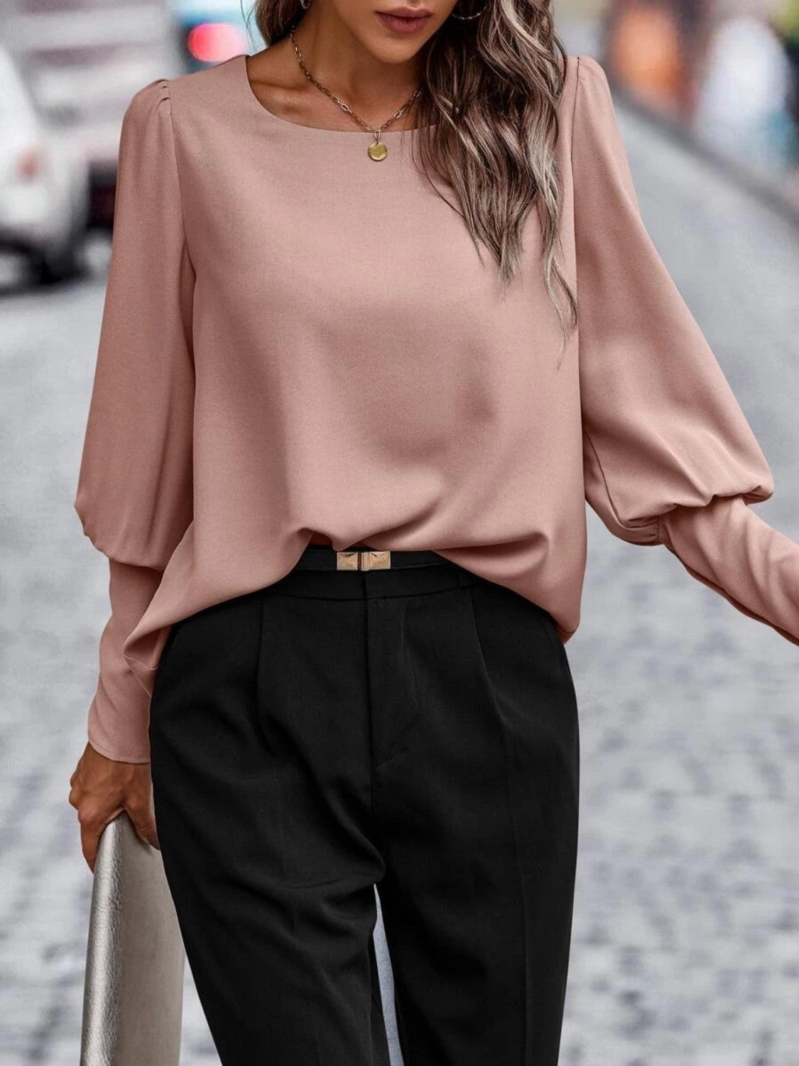 Woman wearing a blush pink long sleeve blouse with black tailored pants on city street