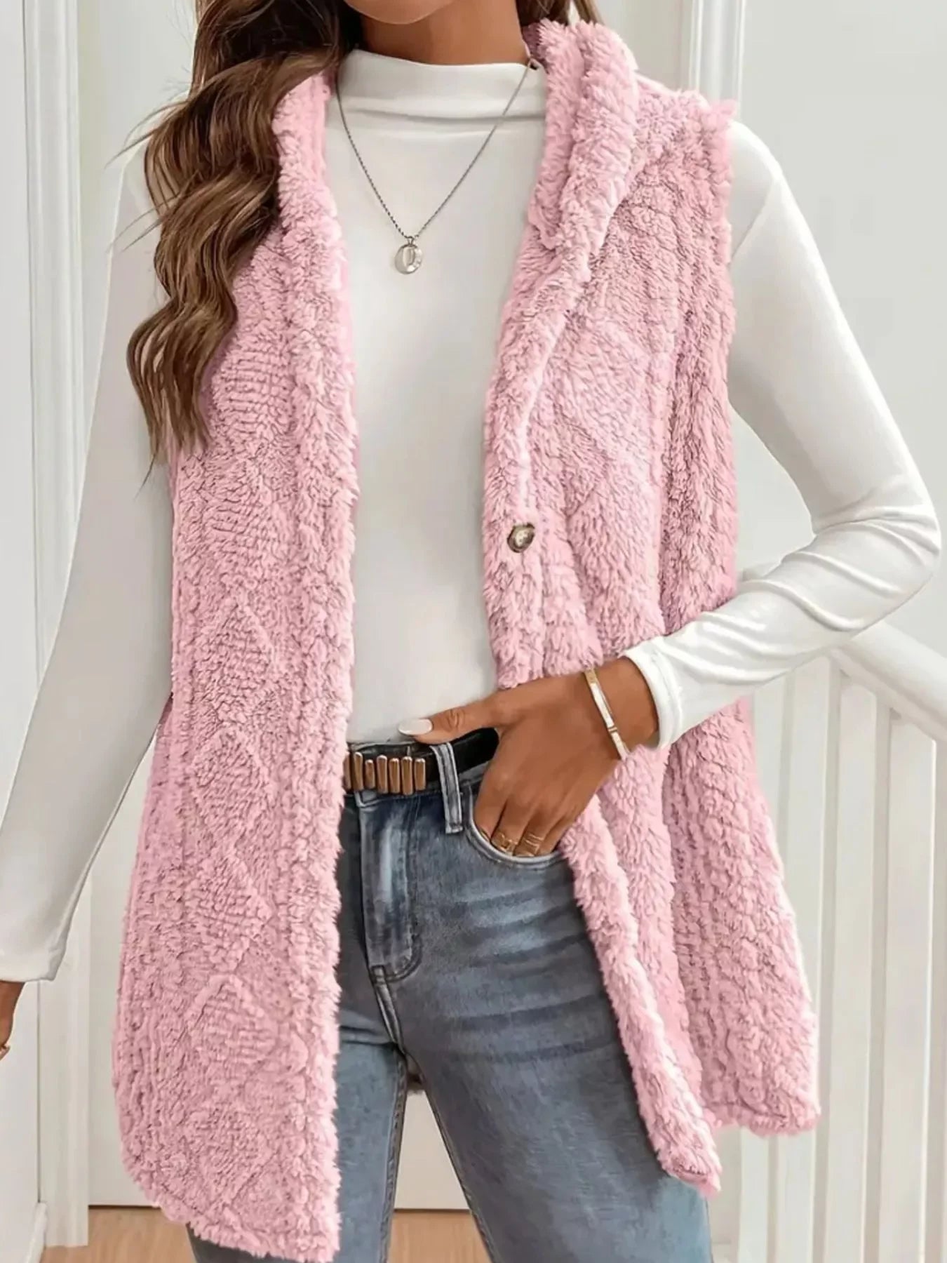 Woman wearing pink textured sherpa vest over white long-sleeve top with blue jeans and silver necklace