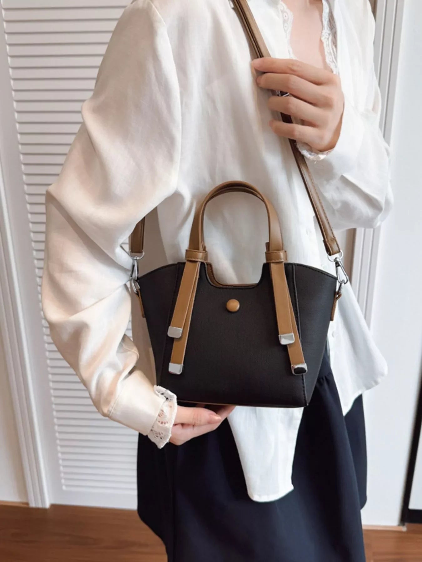 Woman wearing white blouse and black skirt holding black handbag with brown handles and strap