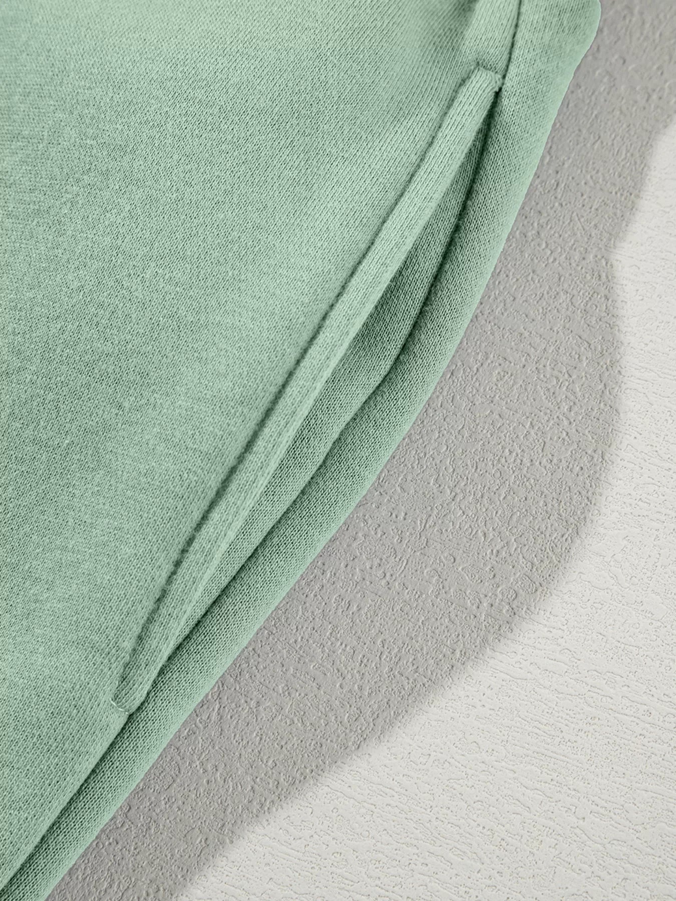 Close-up of mint green knit fabric with a folded edge on textured white surface