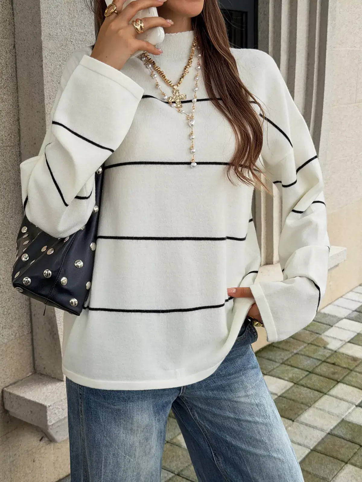 Woman wearing an Evie's Dreamland white striped mock neck sweater with wide sleeves and blue jeans.