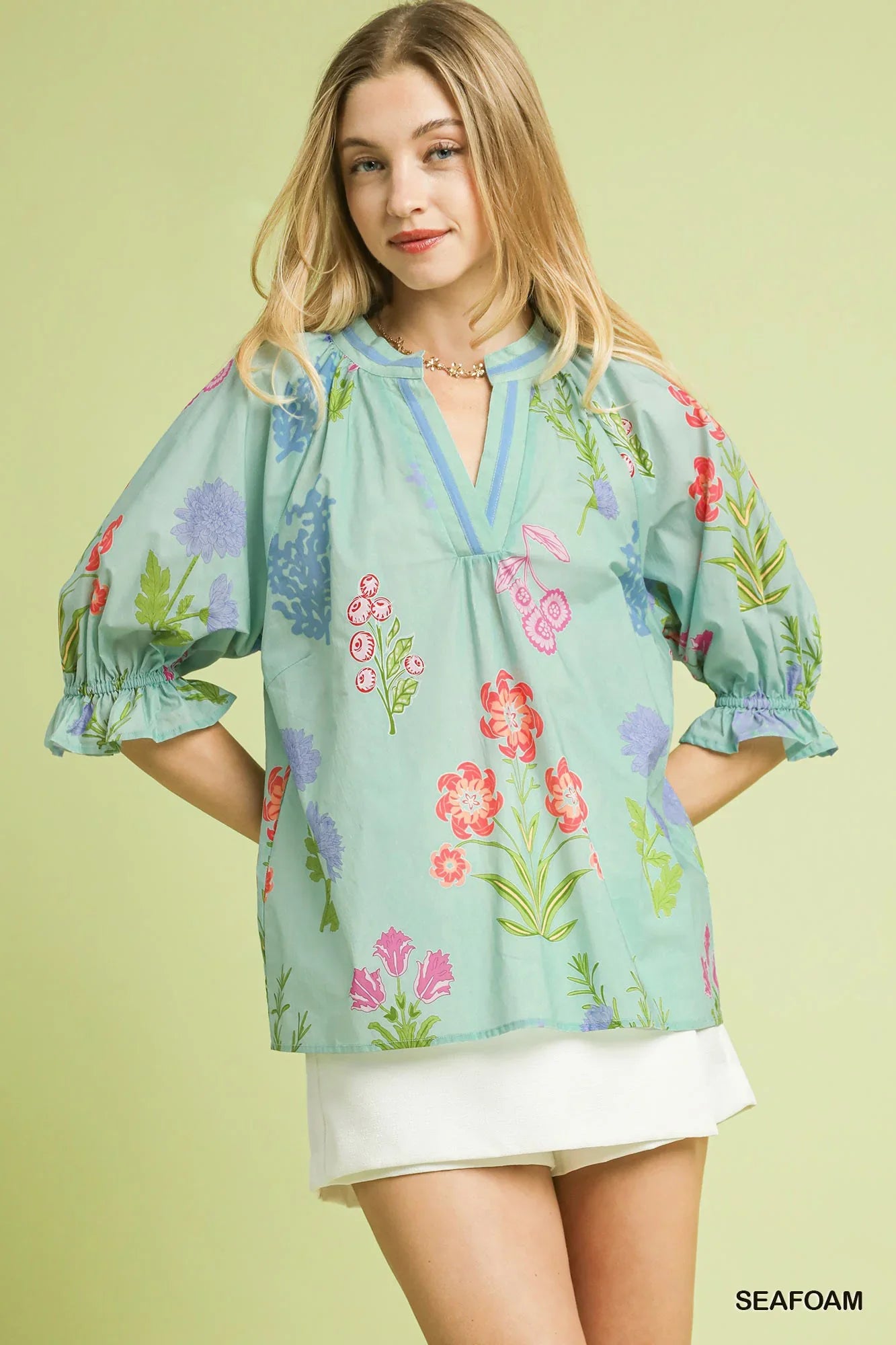 Woman wearing a seafoam green floral blouse with puff sleeves and white skirt