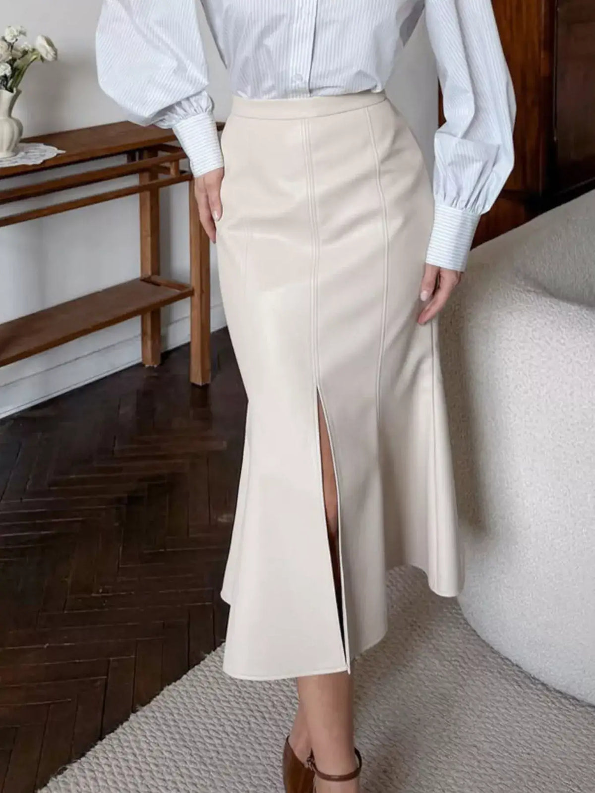 Woman wearing a cream faux leather slit mermaid midi skirt from Evie's Dreamland paired with a blue striped shirt.