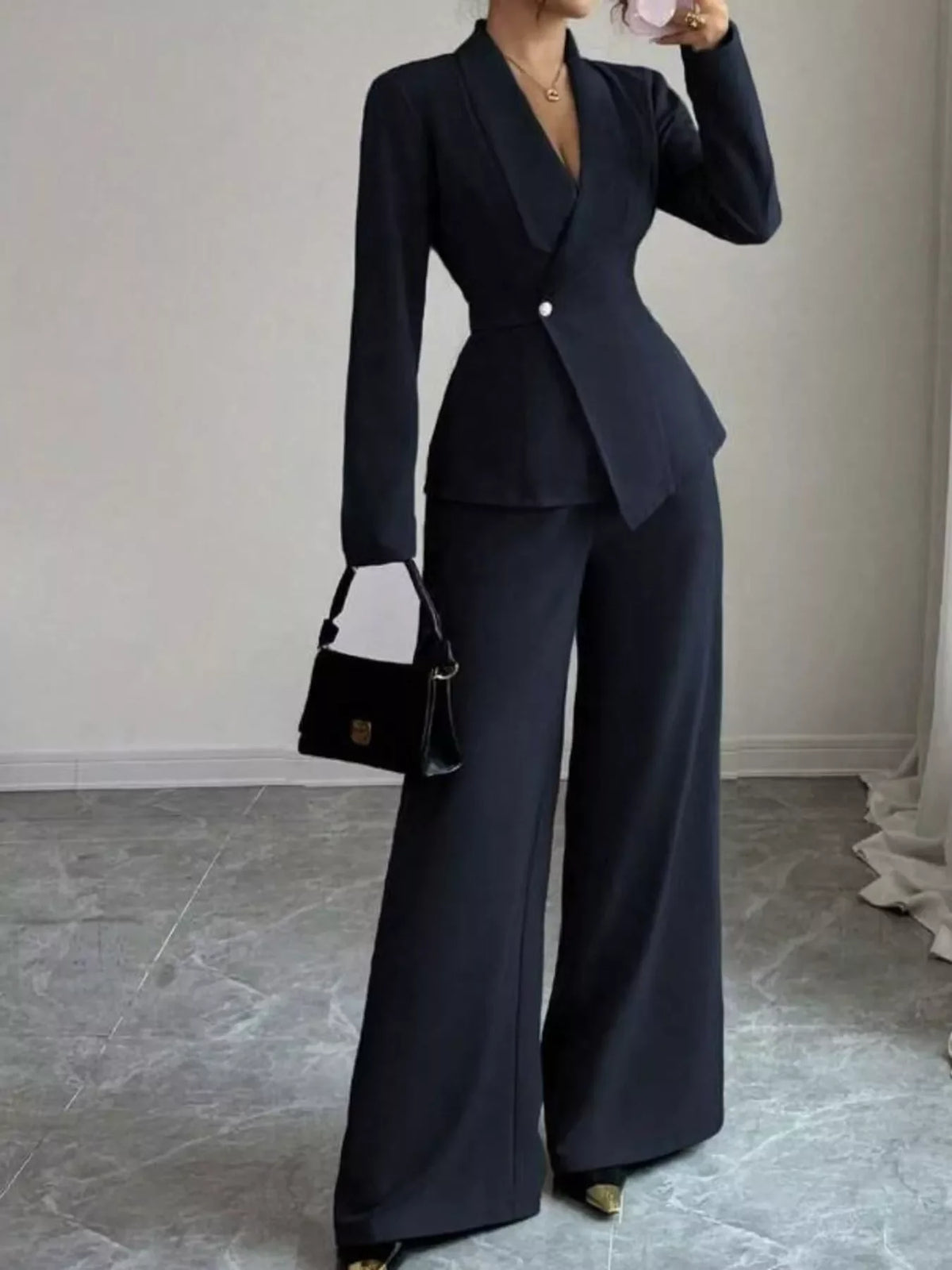 Woman wearing a tailored black pantsuit with wide-leg trousers, holding a black handbag.