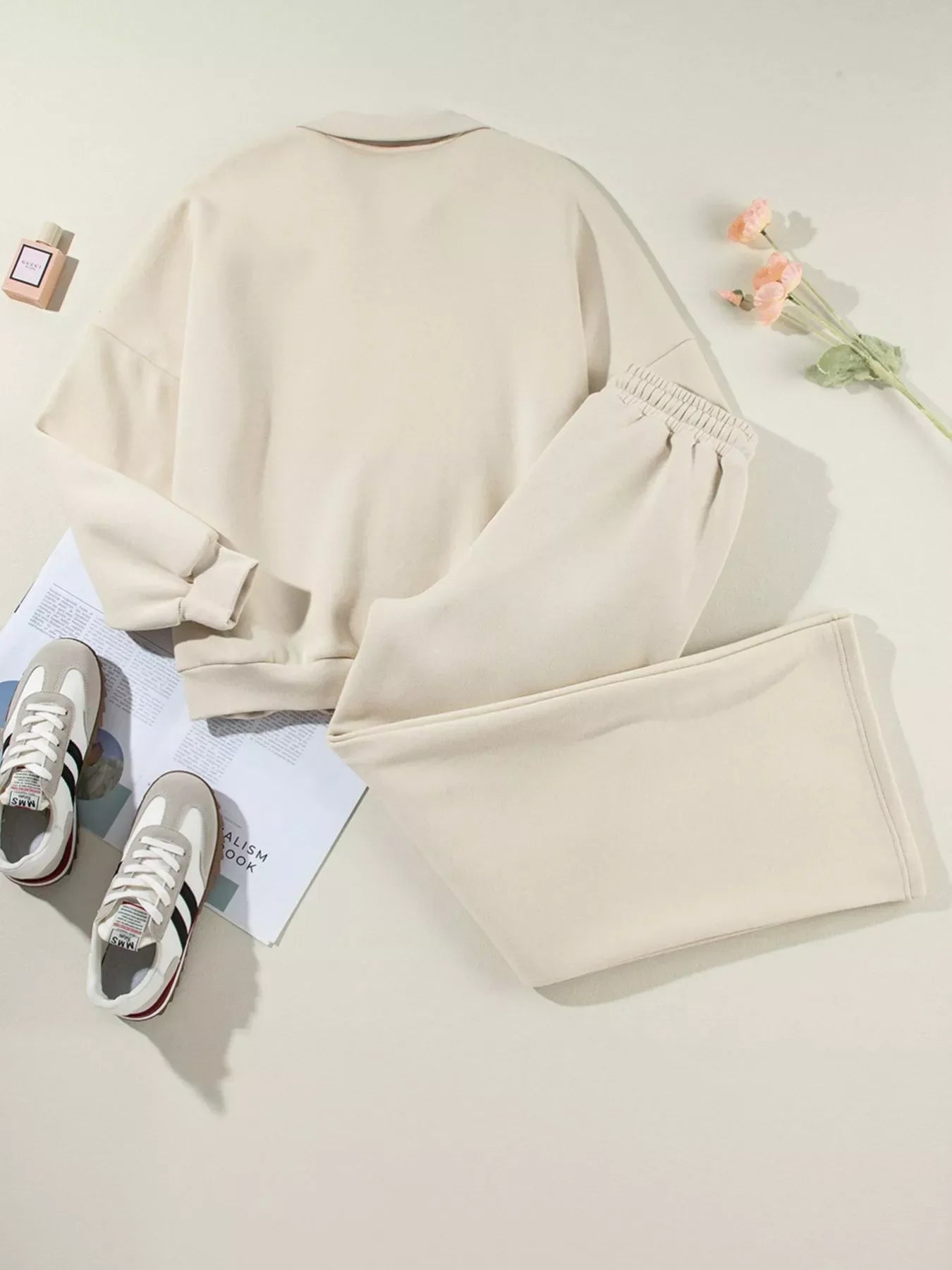 Beige sweatshirt and matching sweatpants with sneakers, perfume, and flowers on white background