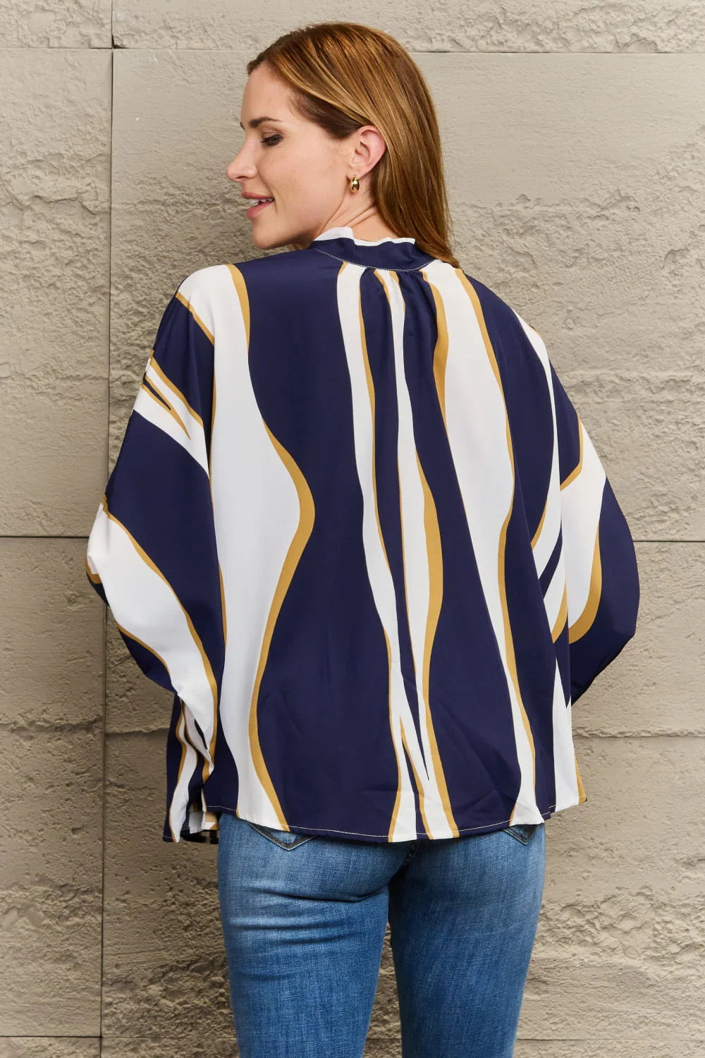 Woman wearing a loose navy, white, and gold striped blouse with blue jeans
