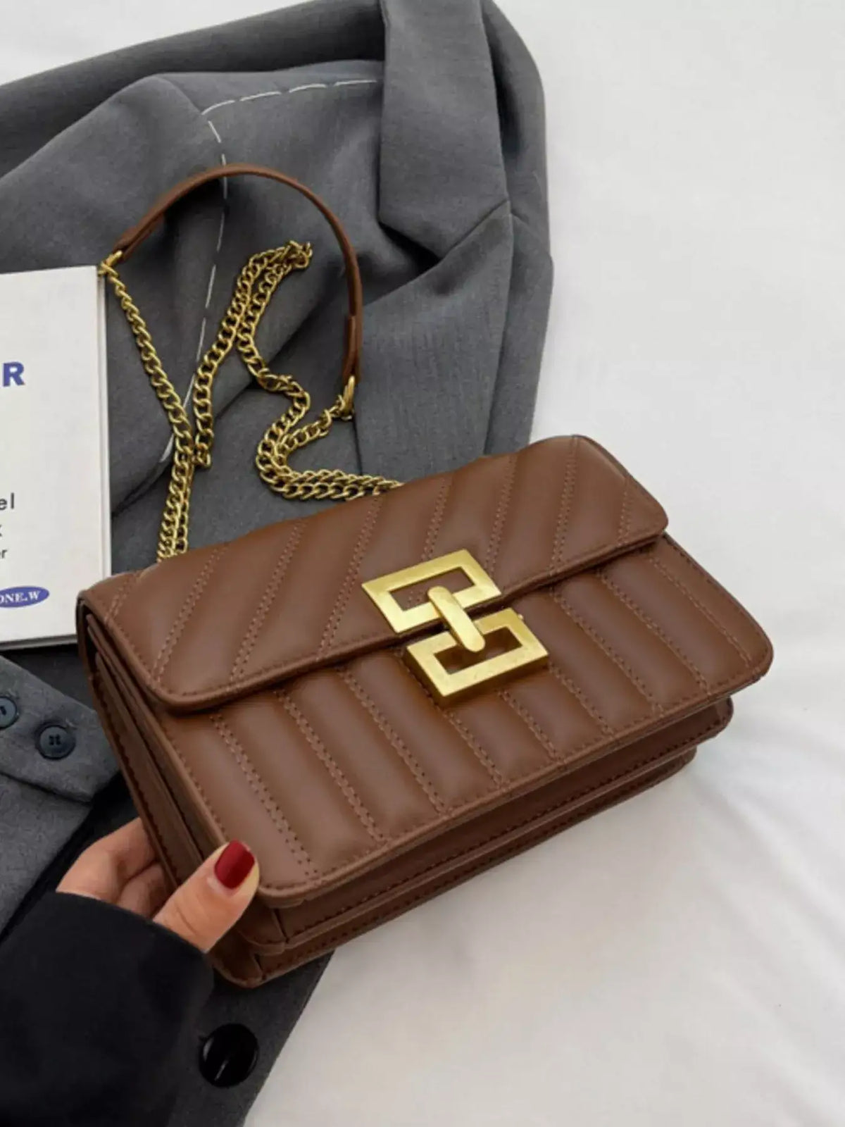 Brown quilted flap chain shoulder bag by Evie's Dreamland with a gold clasp, paired with a grey blazer.