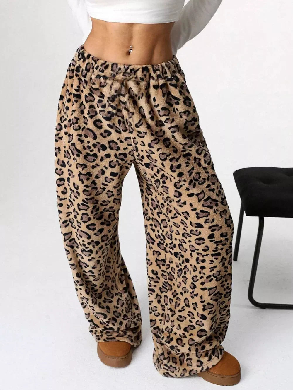Woman wearing cozy leopard print fleece pants with an elastic waistband and brown slippers