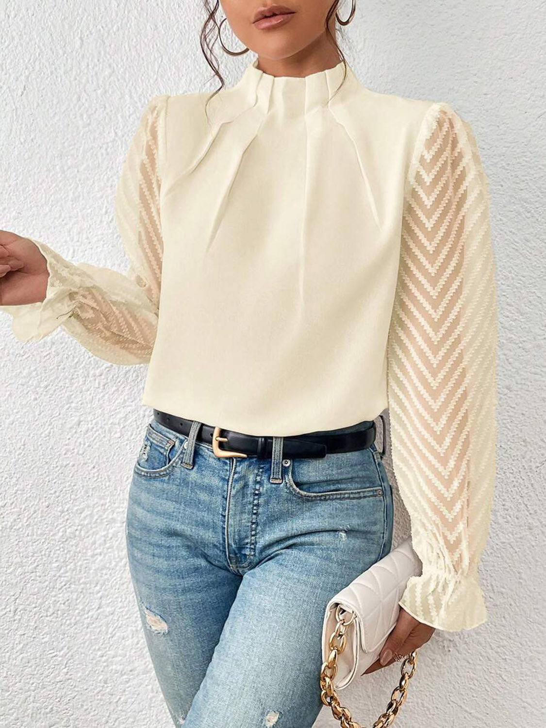 Woman in sheer chevron-sleeve cream blouse, distressed jeans, holding quilted chain clutch