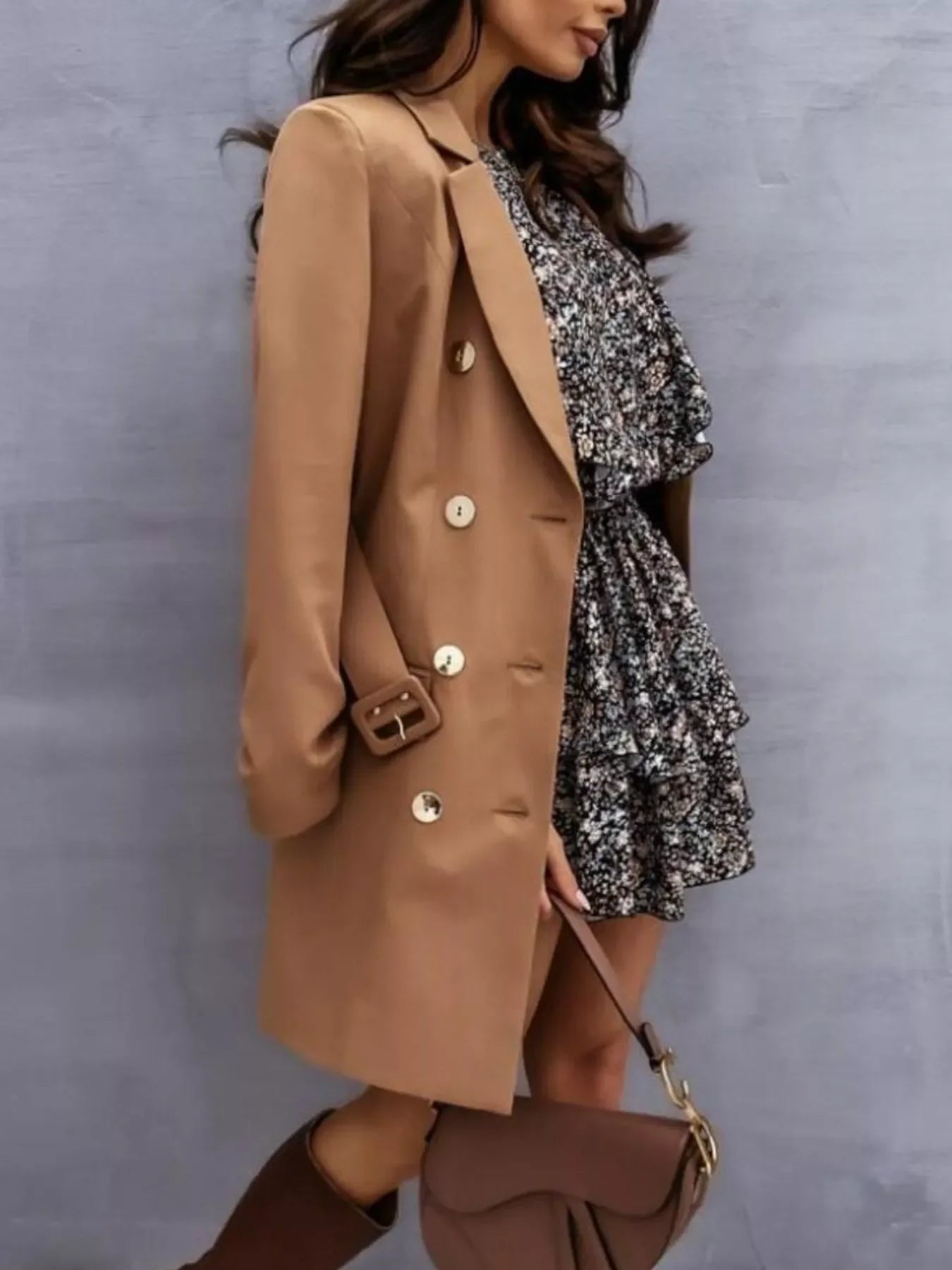 Woman wearing brown double-breasted coat, floral ruffled dress, brown boots, and holding brown handbag