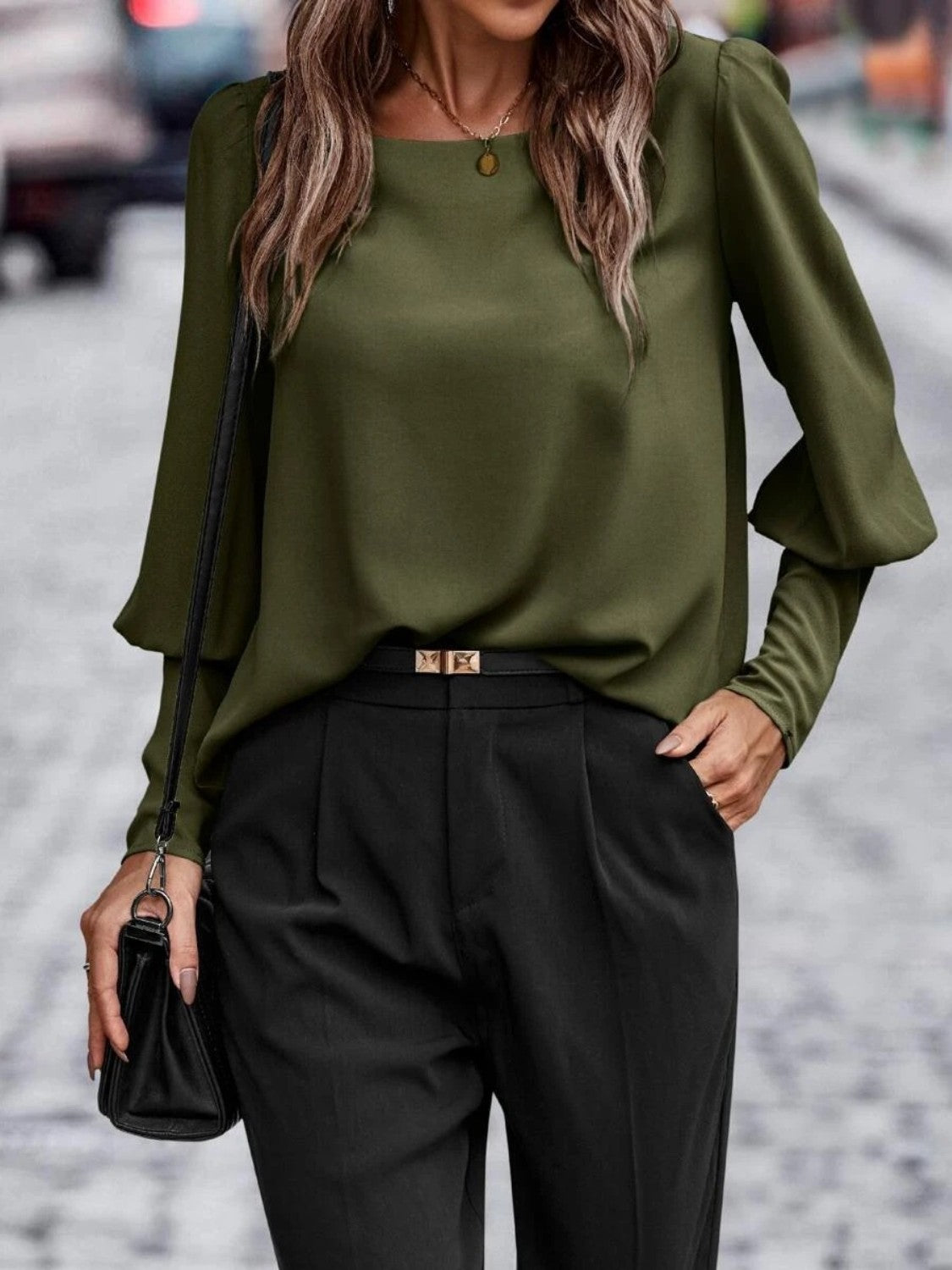Woman wearing an olive green long sleeve blouse with black trousers and handbag on city street