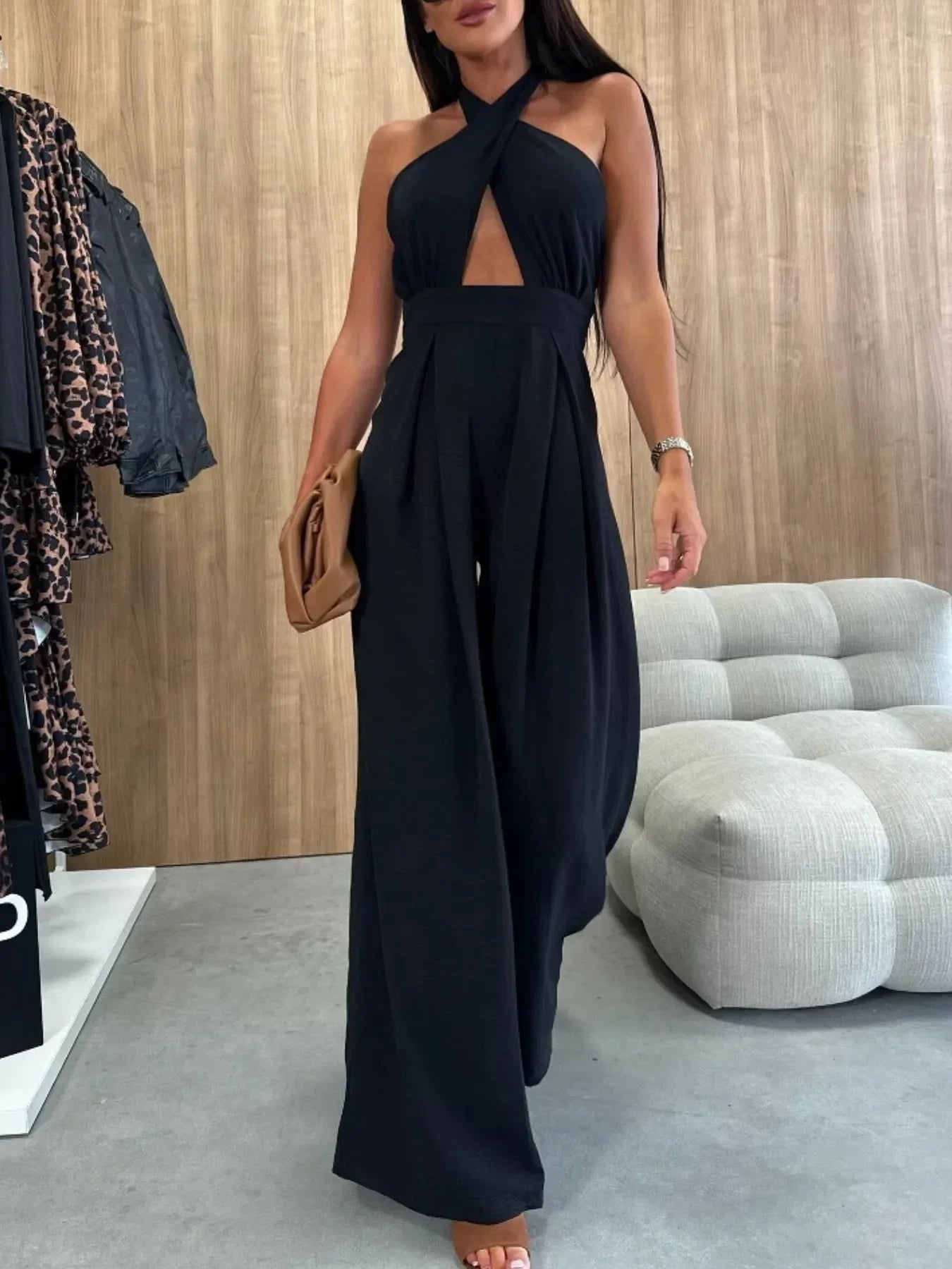 woman wearing black halter neck wide leg jumpsuit holding brown clutch in modern room