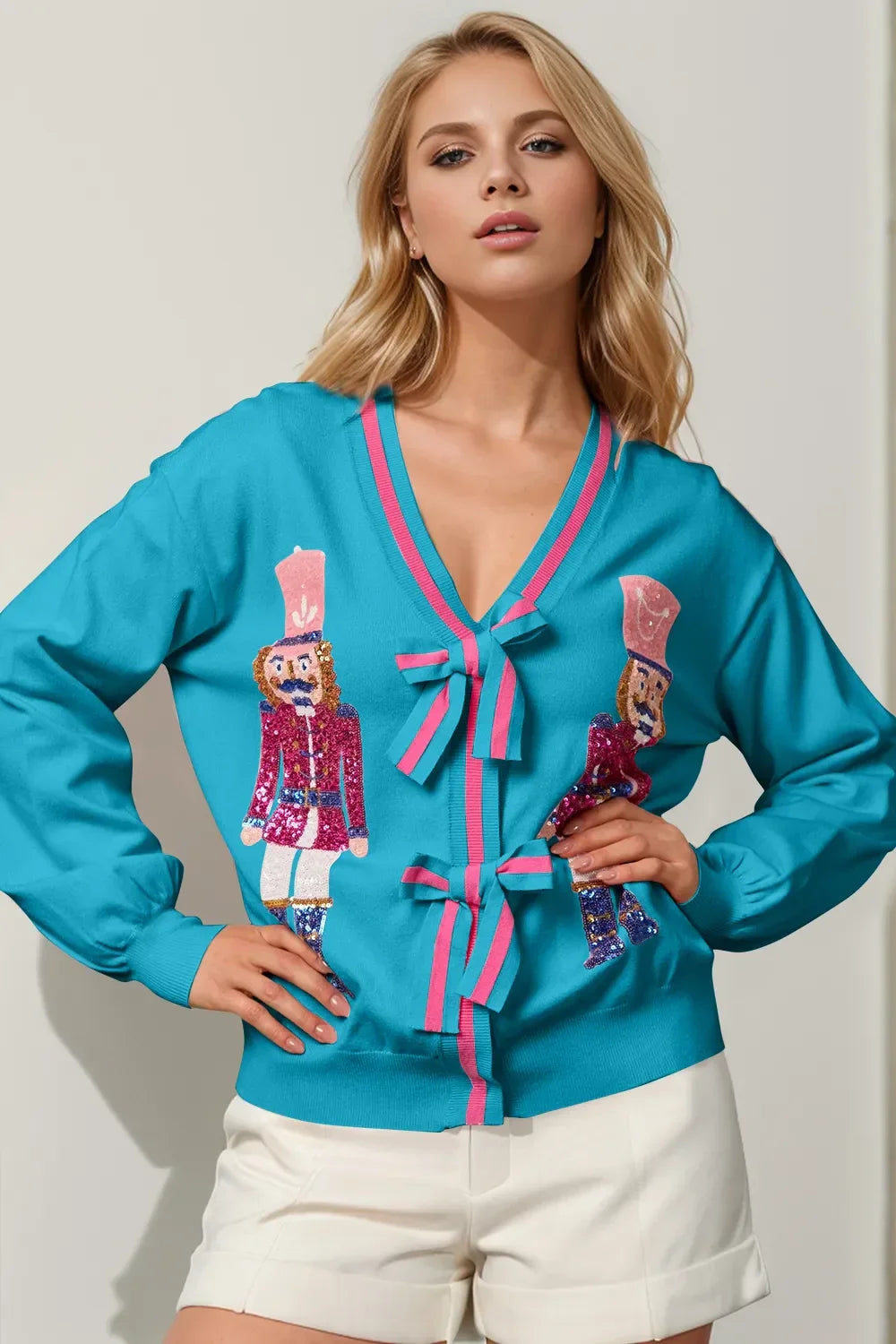 Blonde woman wearing turquoise cardigan with pink bows and nutcracker soldier sequin designs, paired with white shorts