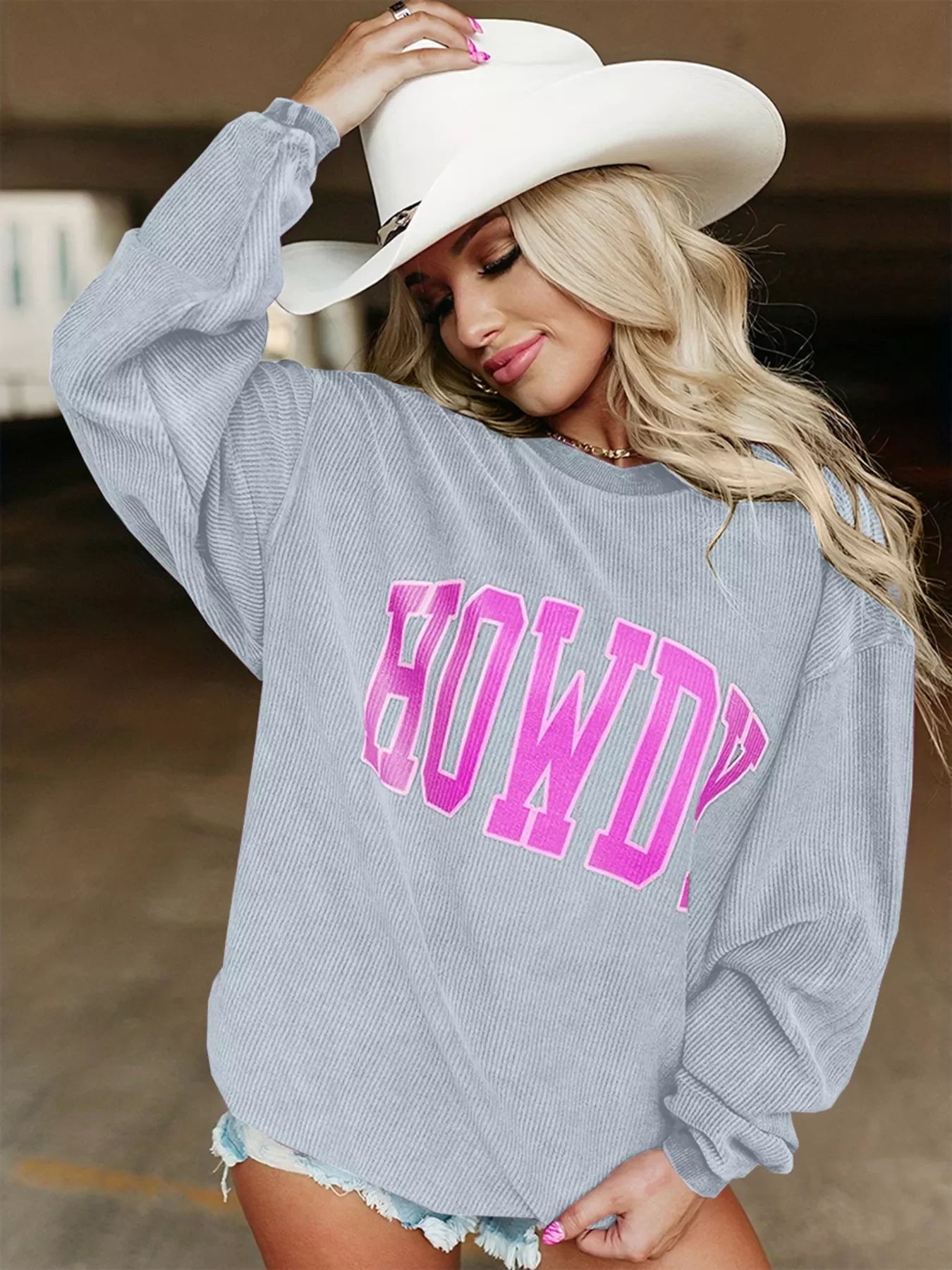 Blonde woman wearing gray sweater with pink HOWDY text and white cowboy hat