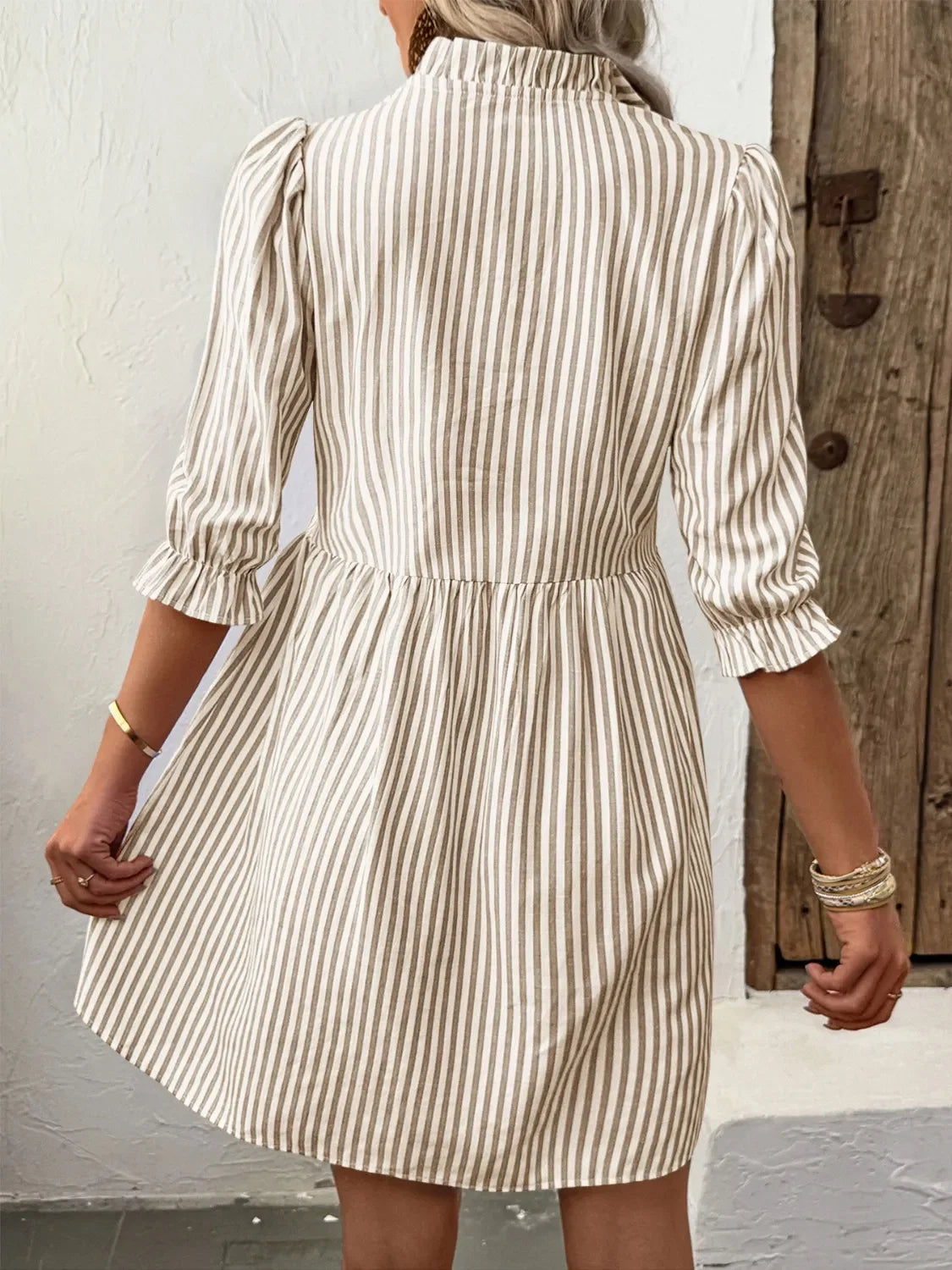Back view of woman wearing beige and white vertical striped dress with puff sleeves and bracelets