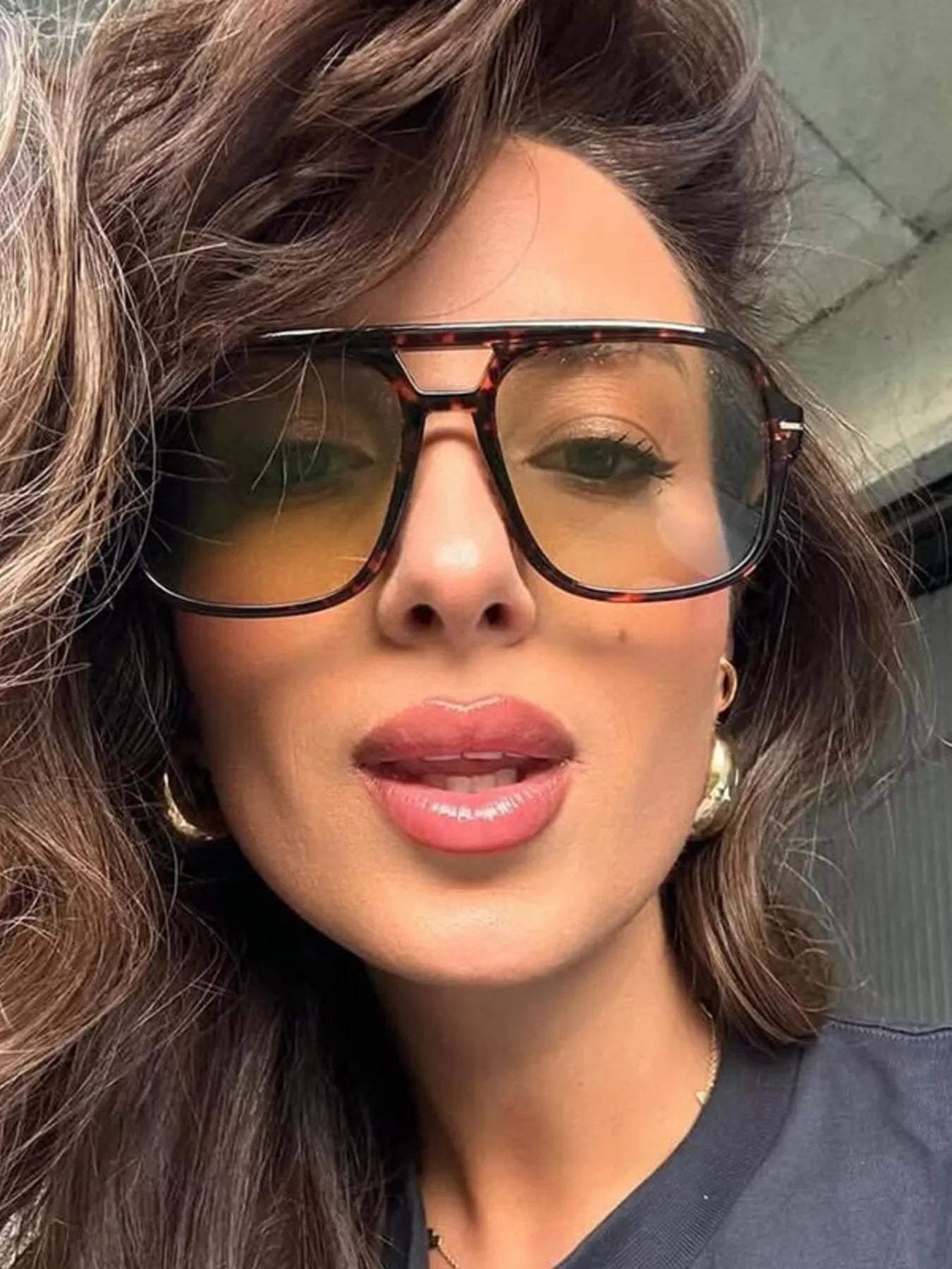 Woman wearing oversized tortoise shell sunglasses with yellow tinted lenses and gold hoop earrings