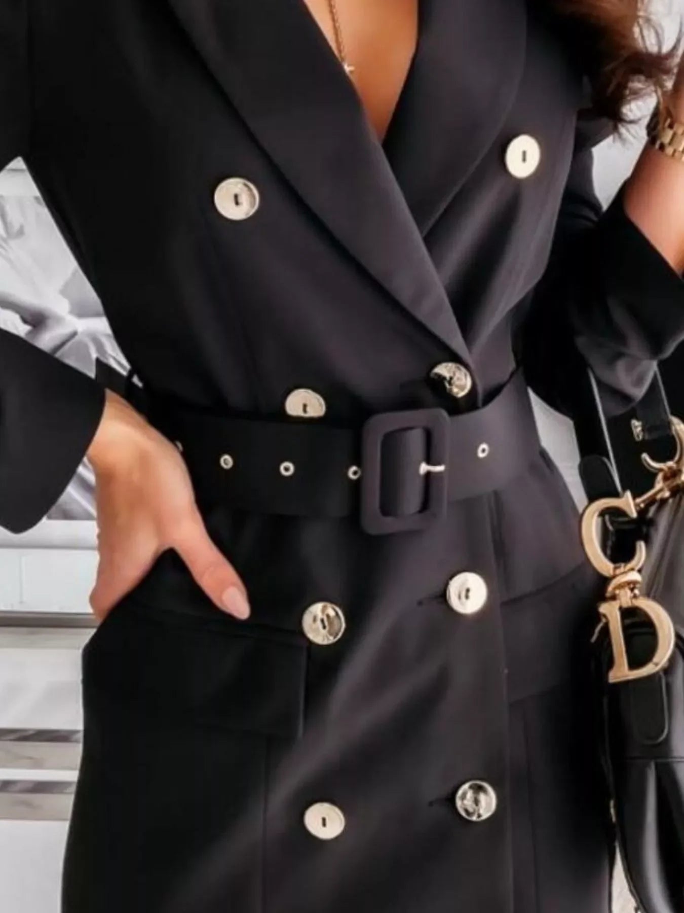 Woman wearing black double-breasted blazer dress with silver buttons, black belt, and carrying black handbag with gold charm