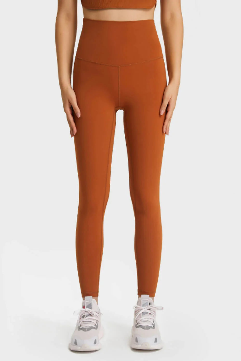 Front view of woman wearing high-waisted rust orange leggings with white athletic sneakers