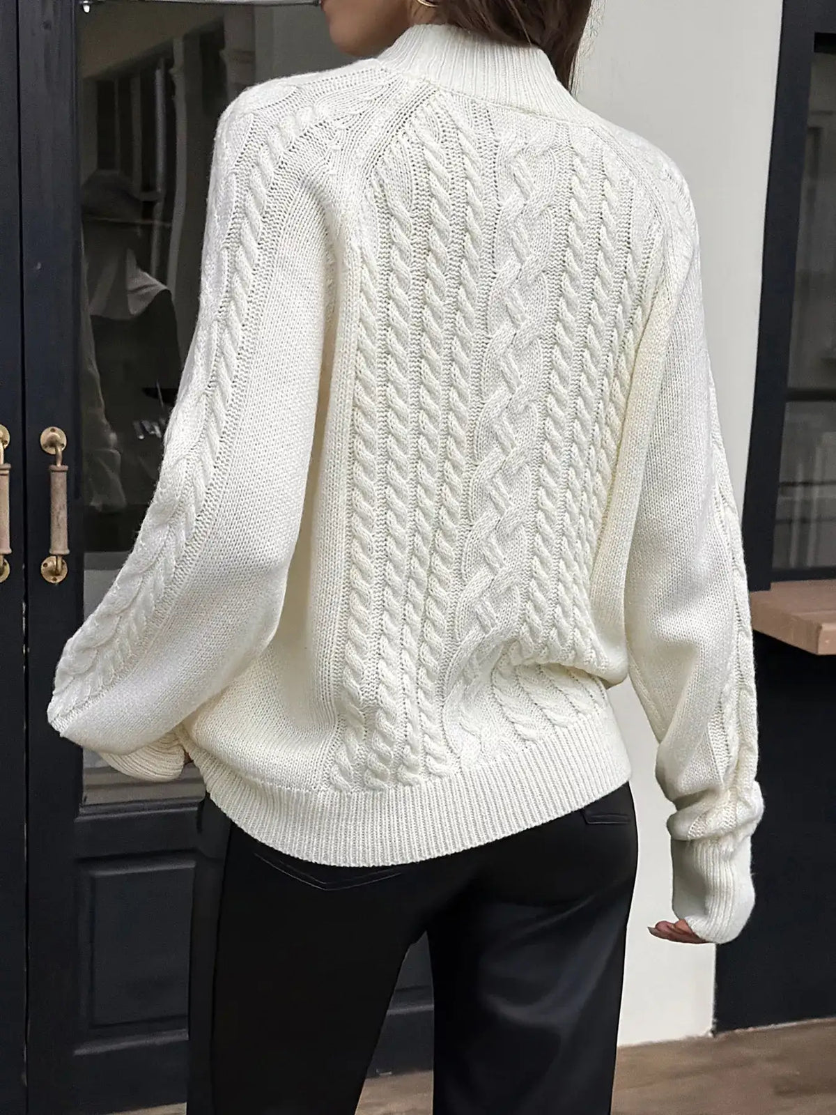 Back view of a white mock neck cable-knit sweater by Evie's Dreamland paired with black leather pants.