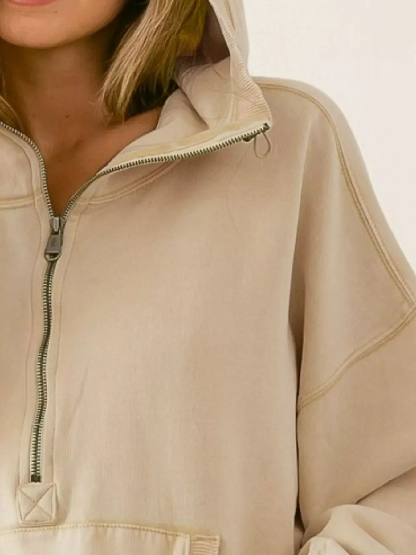 Close-up of person wearing beige half-zip hoodie with a hood and visible stitching details