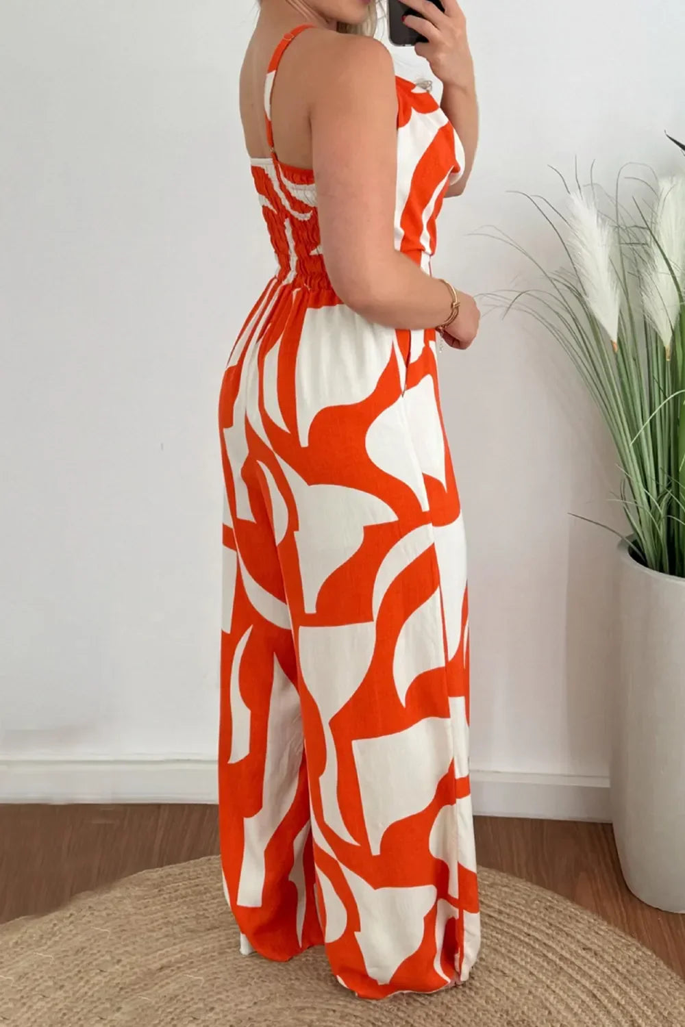 Woman wearing orange and white abstract print sleeveless jumpsuit standing indoors