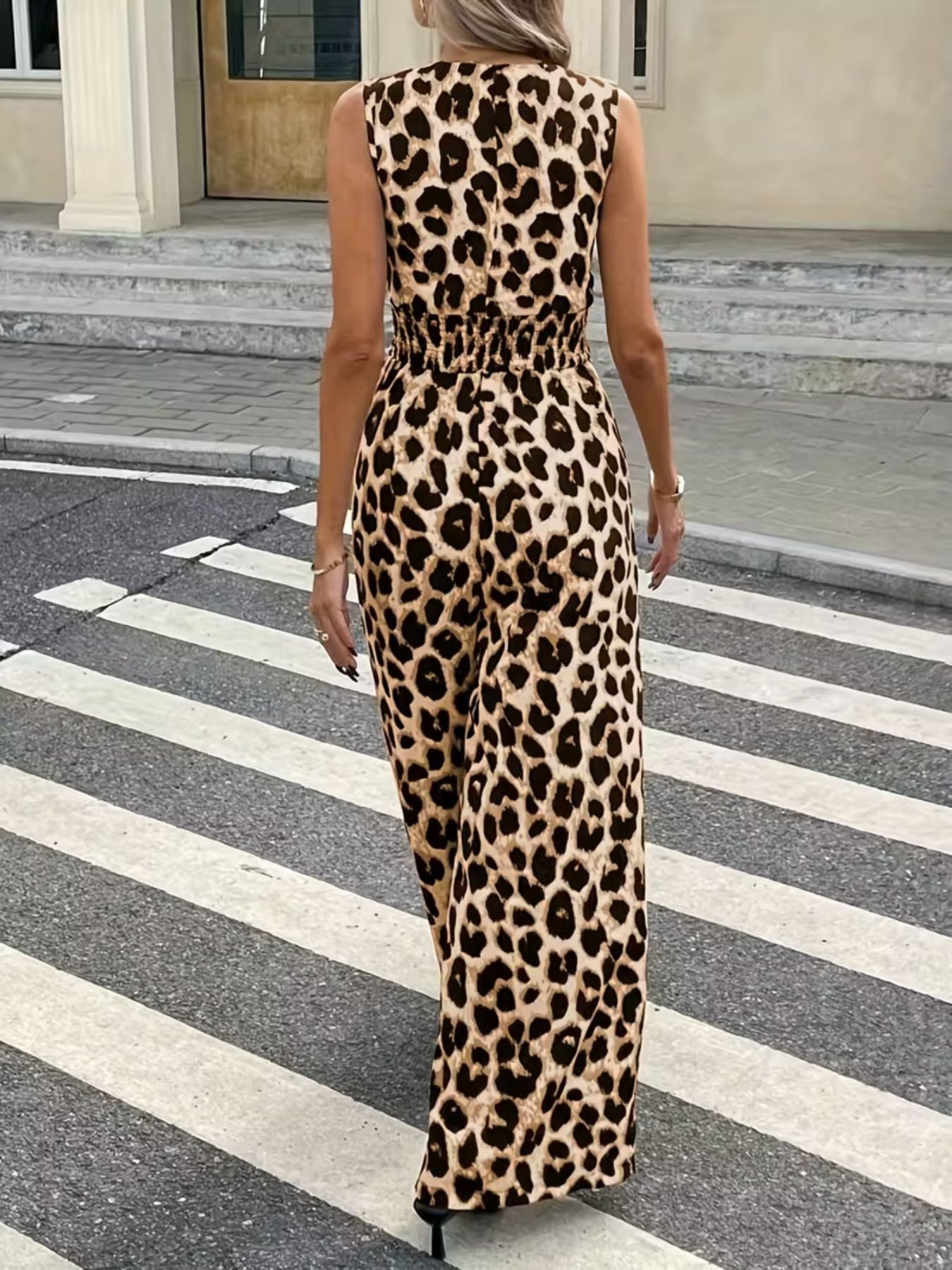 Woman in leopard print sleeveless jumpsuit walking on city crosswalk