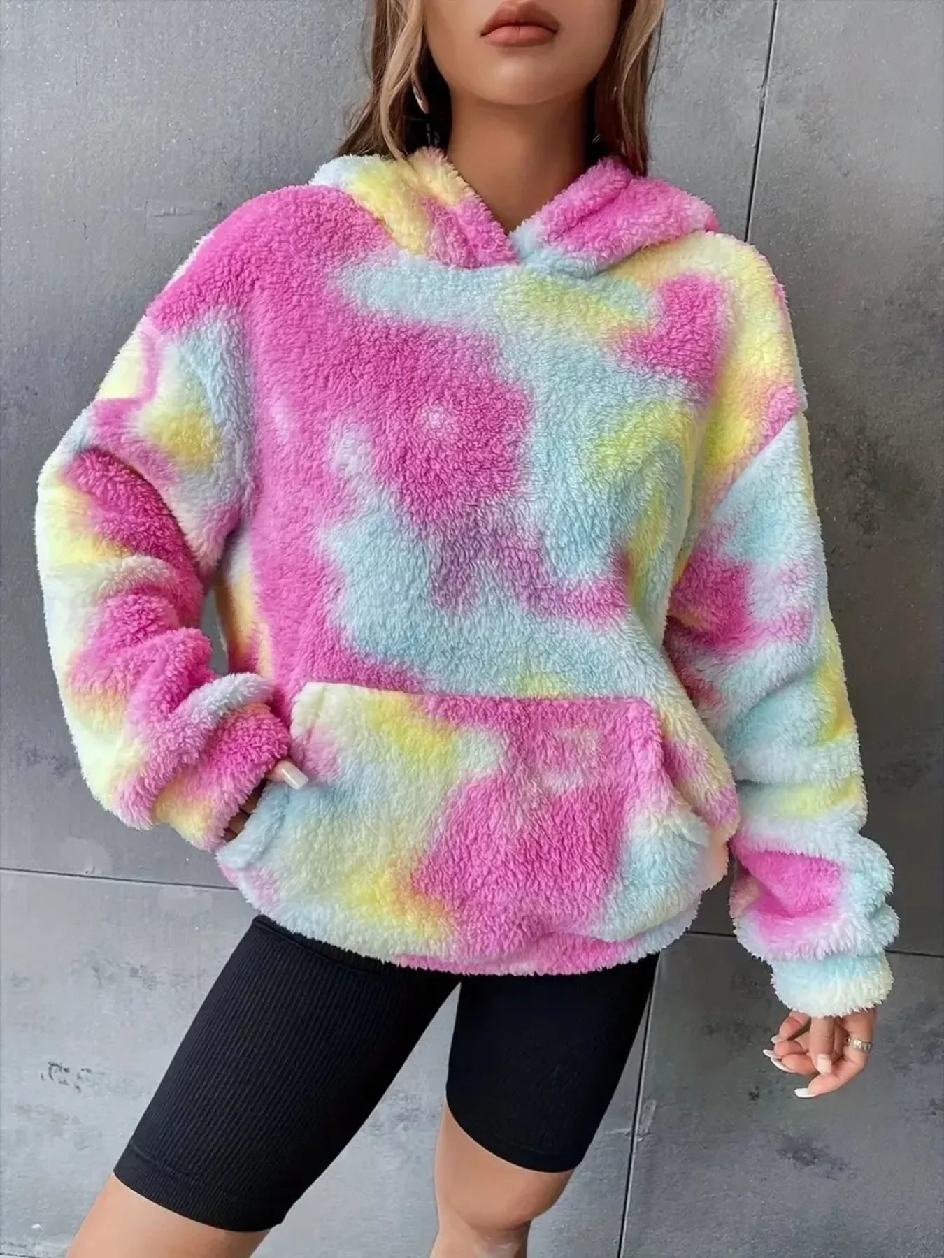 Woman wearing a colorful fuzzy pastel tie-dye hoodie with black cycling shorts against gray wall