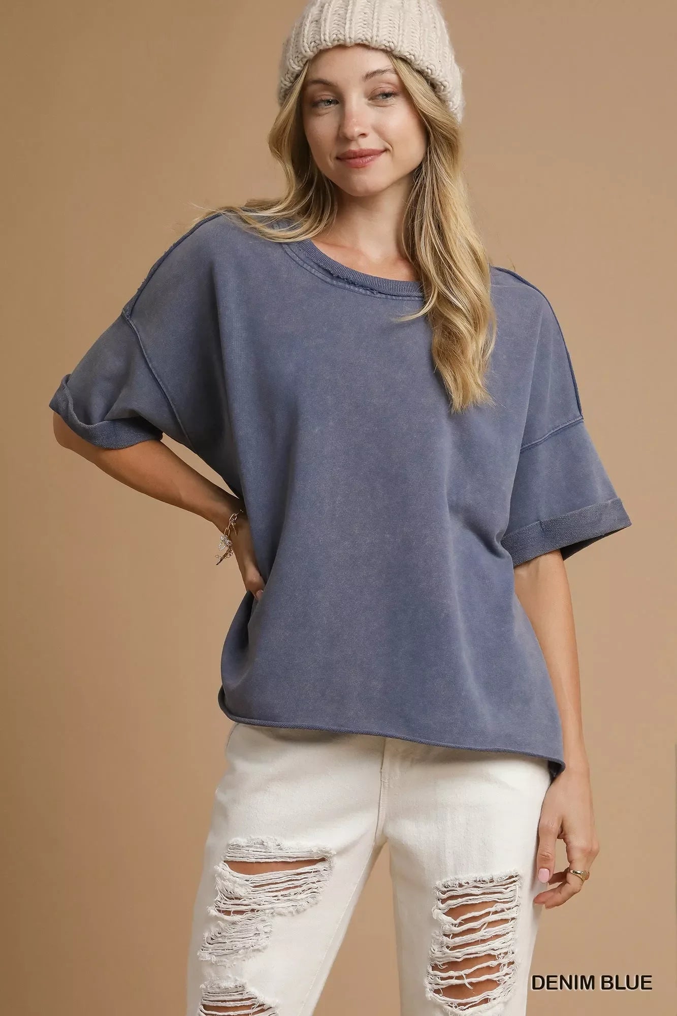 Young woman wearing denim blue oversized short-sleeve shirt, cream knit beanie, and white ripped jeans