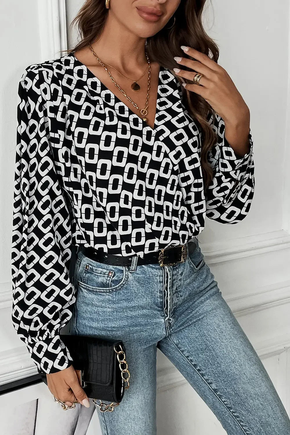 Woman wearing black and white geometric print blouse with puff sleeves, light blue jeans, gold jewelry, and holding black handbag