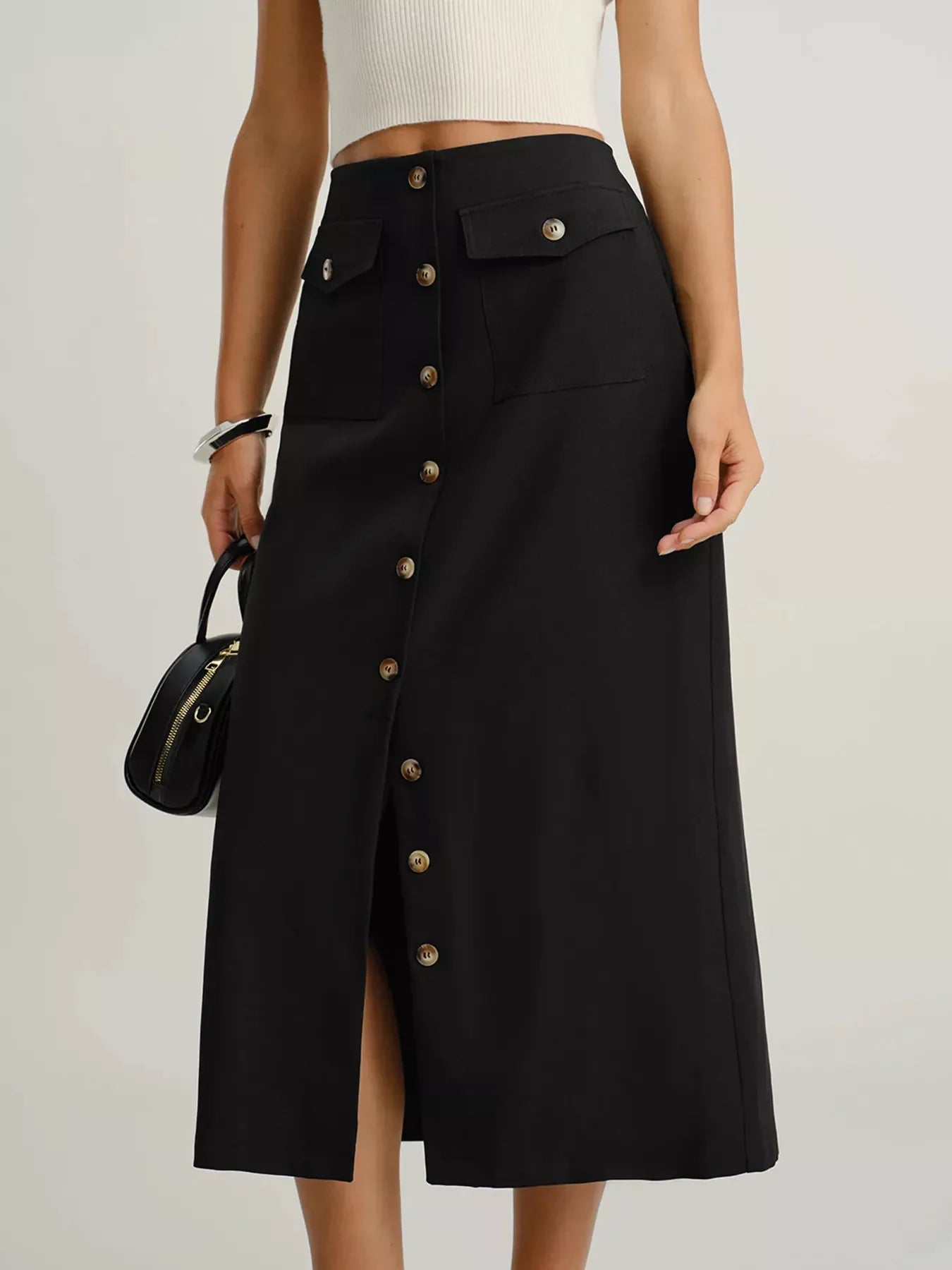Woman wearing high-waisted black midi skirt with front buttons and flap pockets