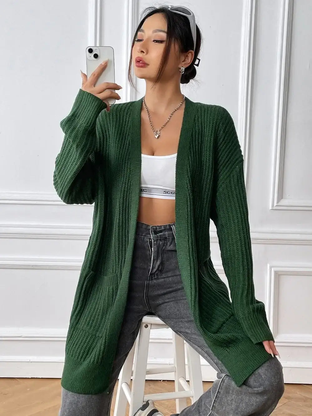 Woman wearing an Evie's Dreamland green open front long sleeve knit cardigan with grey jeans.