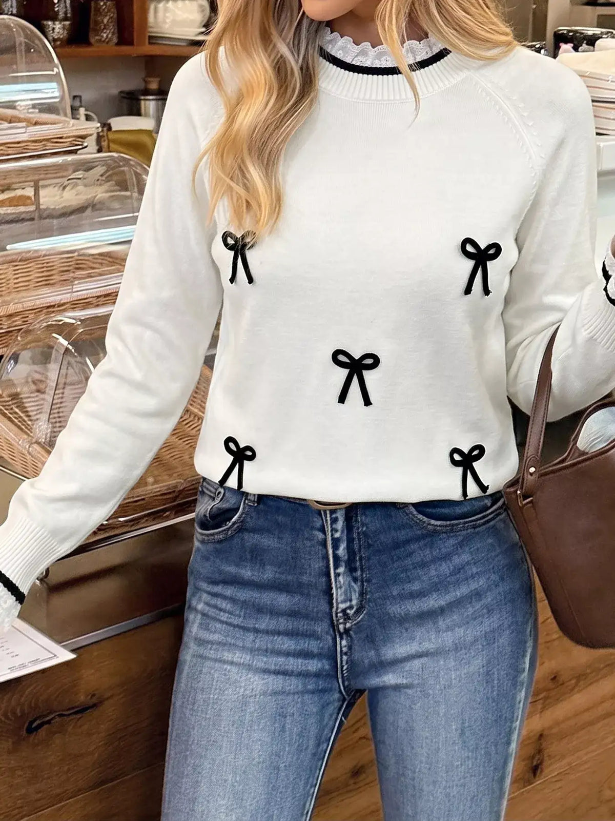 Woman wearing a white Evie's Dreamland bow-embellished sweater with lace trim and blue jeans.