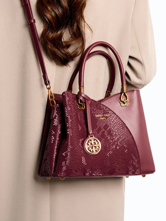 Elegant burgundy snakeskin handbag with gold hardware and crossbody strap on beige coat
