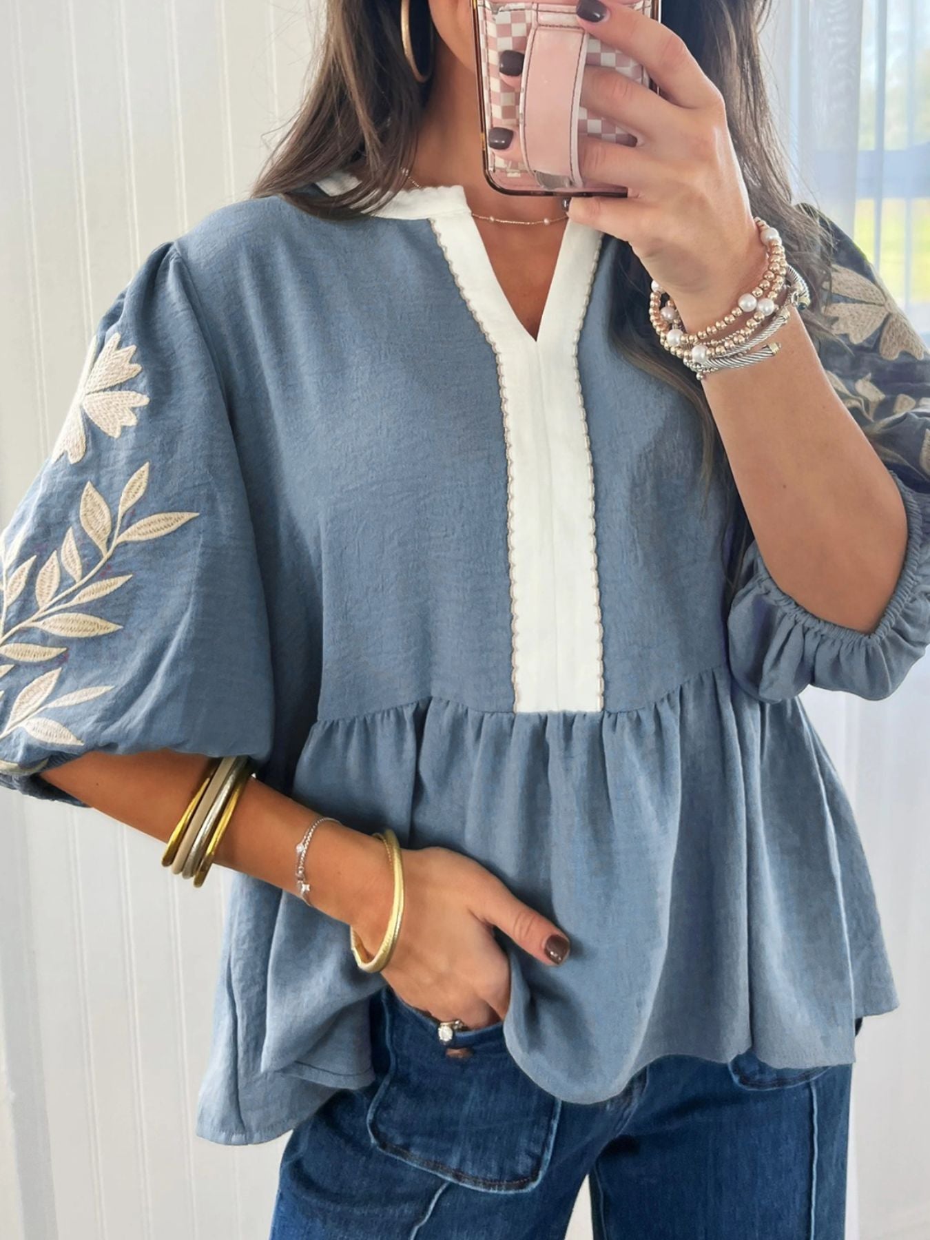 Blue embroidered blouse with white trim, puff sleeves, and peplum hem, styled with jeans and gold jewelry