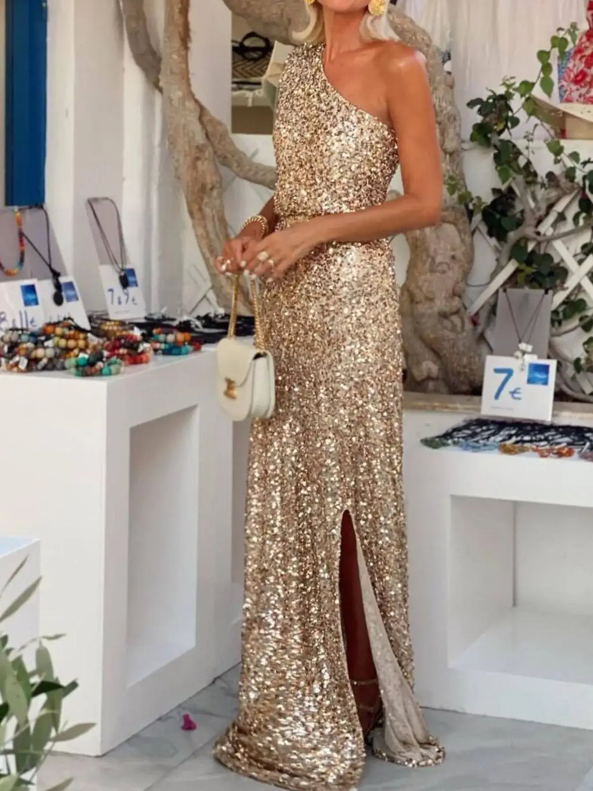 Evie's Dreamland gold sequin one-shoulder maxi dress with a high leg slit and white handbag.