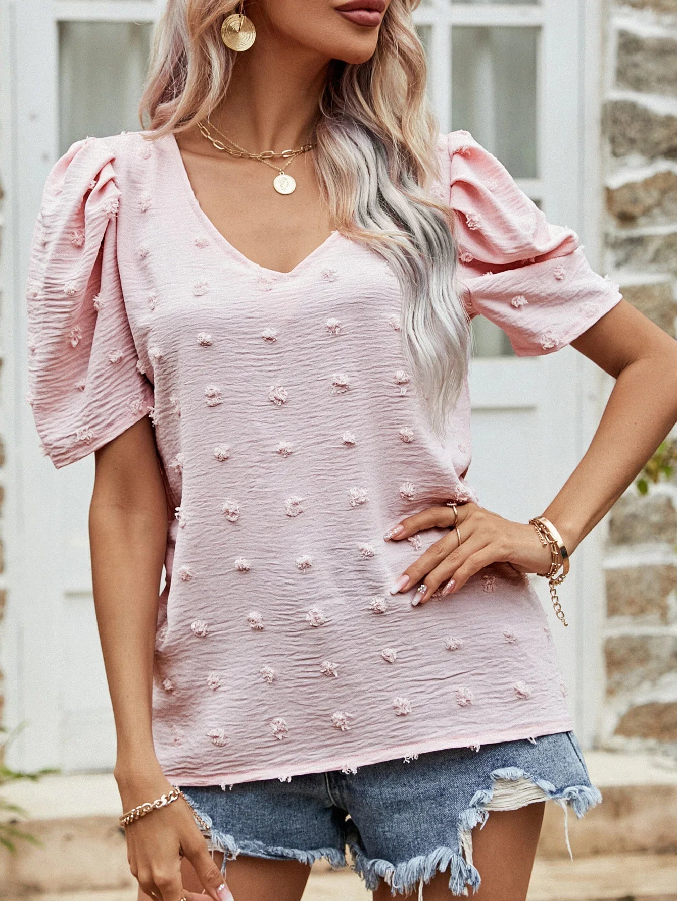 Woman wearing textured pink puff sleeve top and distressed denim shorts with gold jewelry