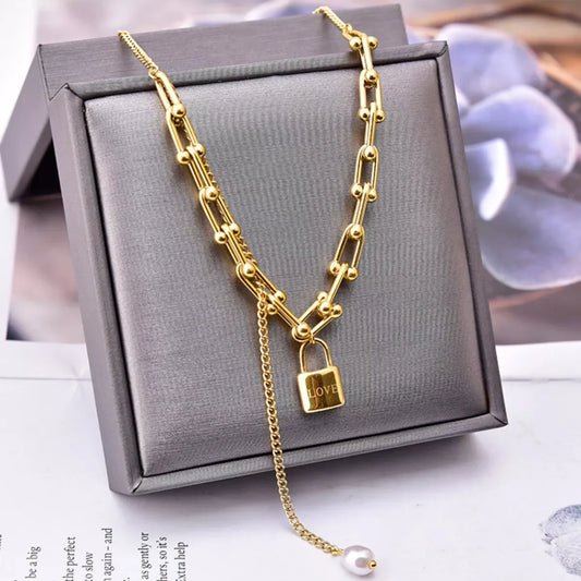 Gold chain necklace with LOVE lock pendant and pearl drop, displayed in gray gift box for elegant fashion accessorizing.