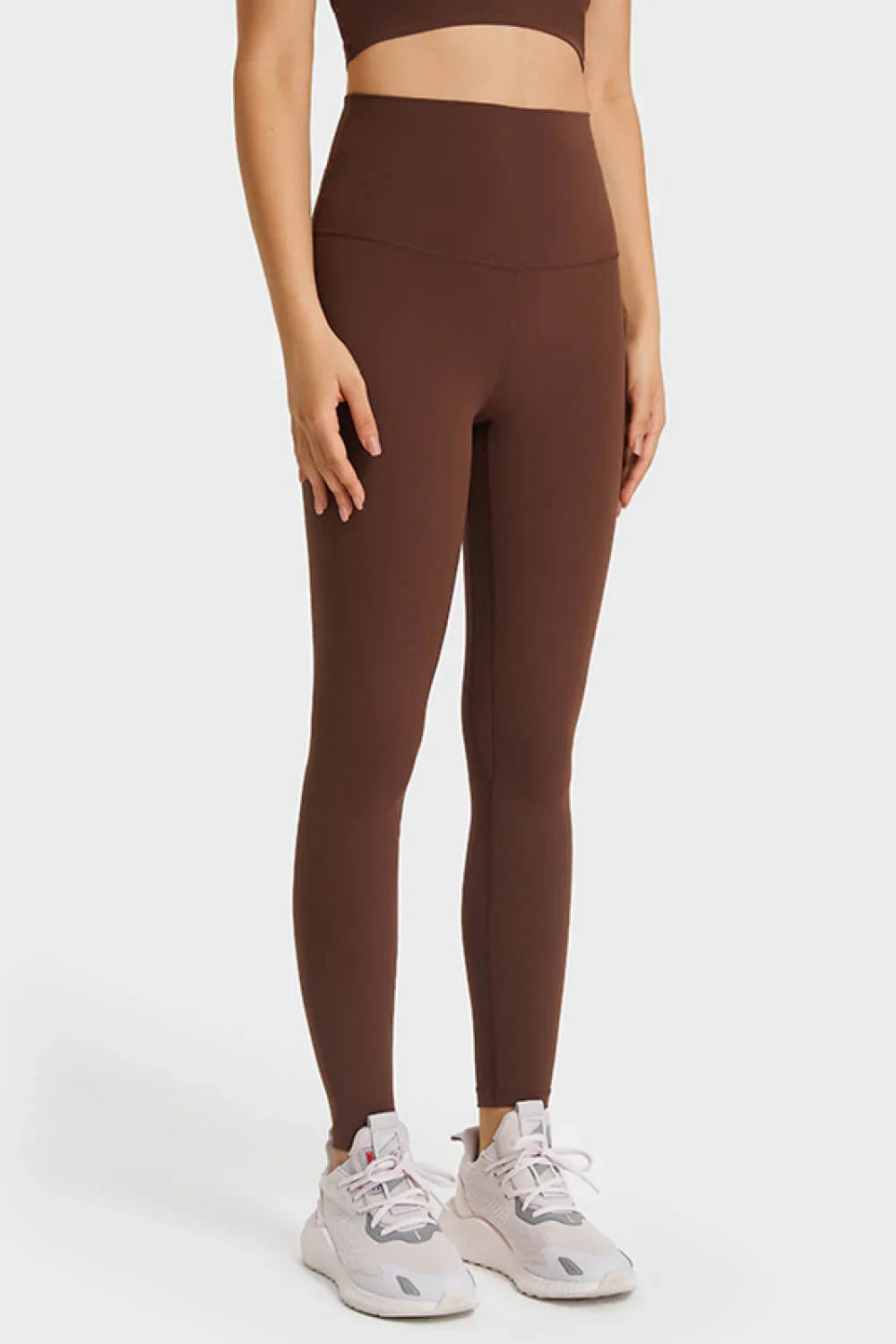 Woman wearing brown high-waisted leggings and white athletic sneakers against a white background