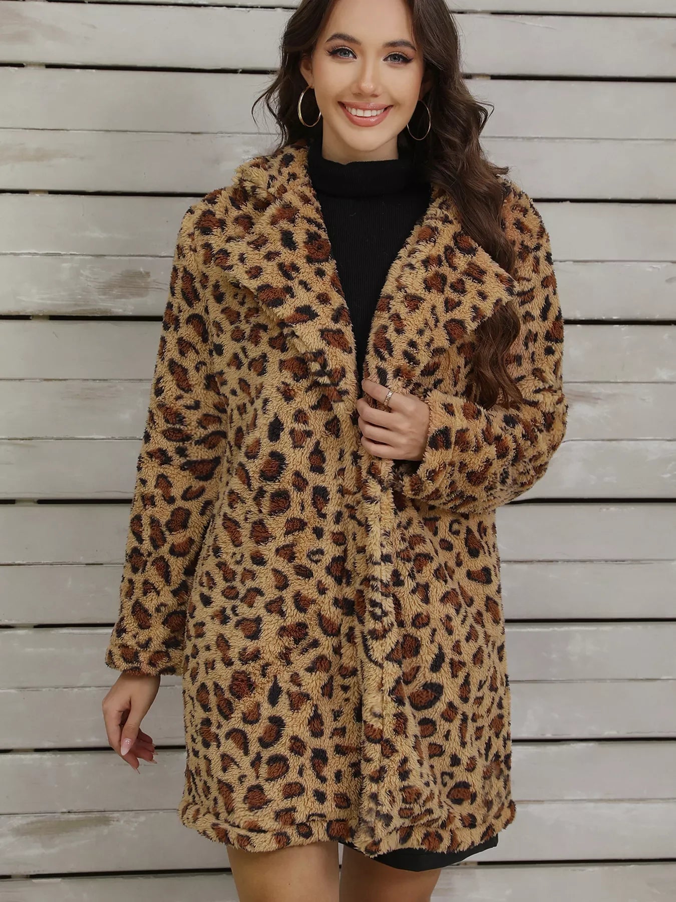 Smiling woman wearing a leopard print faux fur coat over a black dress, standing against a wooden panel wall