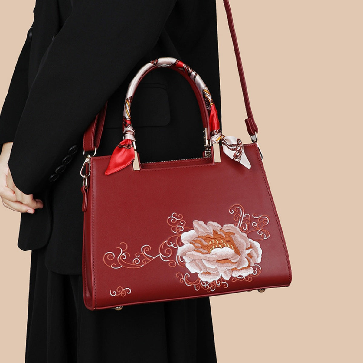 Red floral embroidered handbag with scarf-wrapped handles, held by woman in black outfit