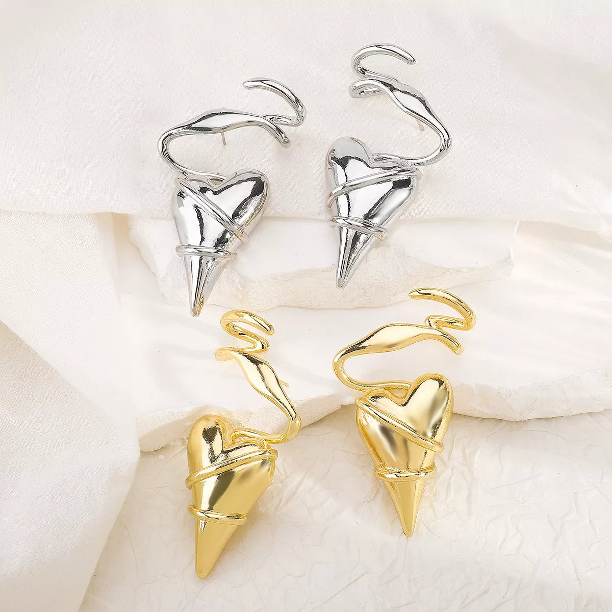 Gold and silver heart-shaped spike earrings with twisted wire design on white fabric