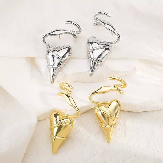 Gold and silver heart-shaped spike earrings with twisted wire design on white fabric