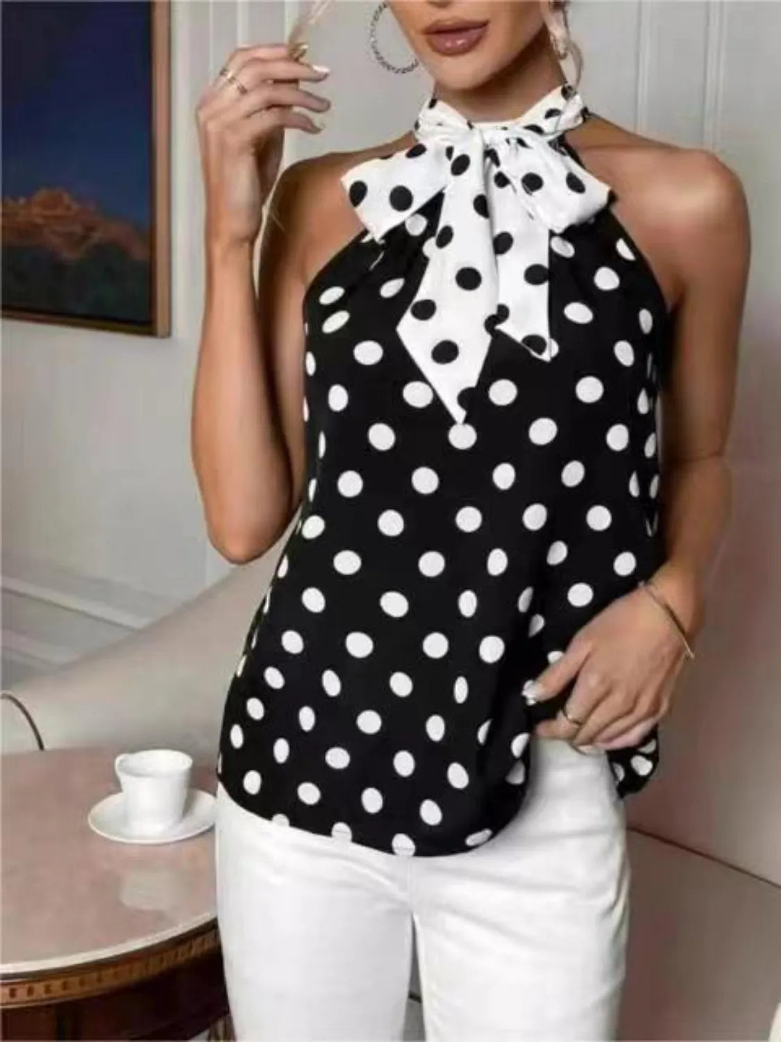Woman wearing a sleeveless black and white polka dot halter top with a bow tie neck