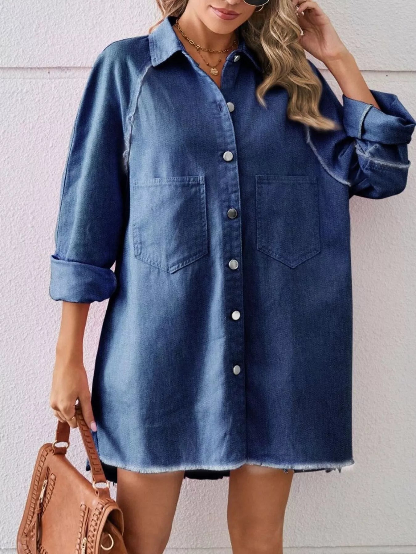 Woman wearing oversized denim shirt dress with front pockets and brown handbag