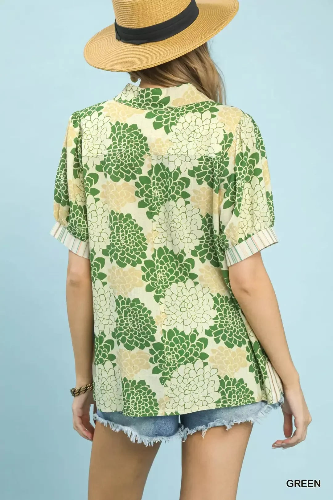 Woman in straw hat wearing green and yellow floral shirt with denim shorts, summer outfit